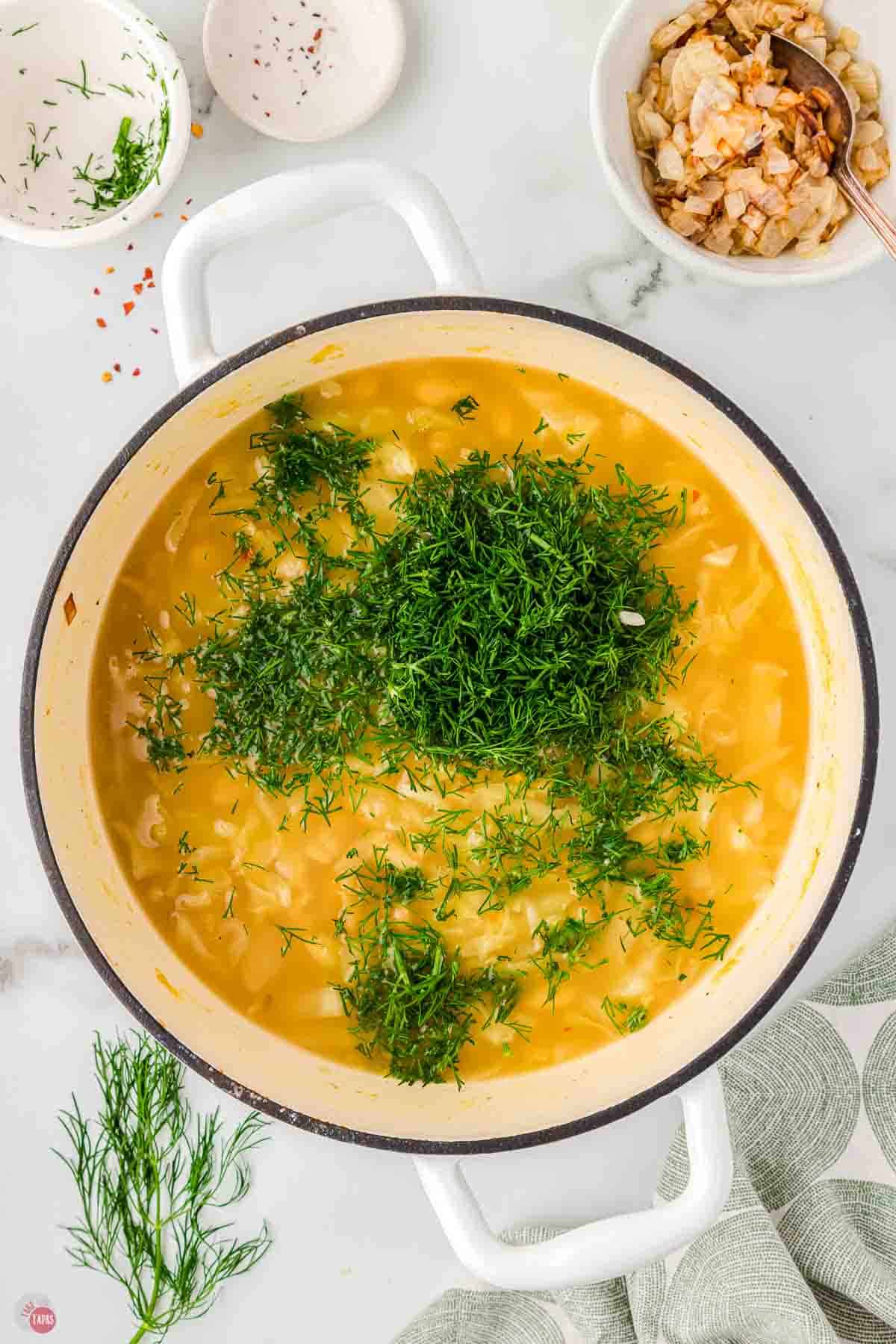 white pot with soup broth and a bunch of chopped fresh dill on top