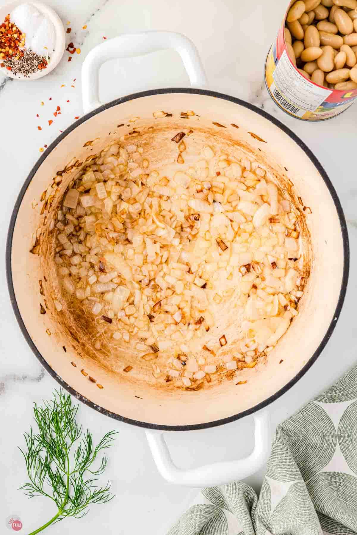 white soup pot with diced onions cooking in the bottom