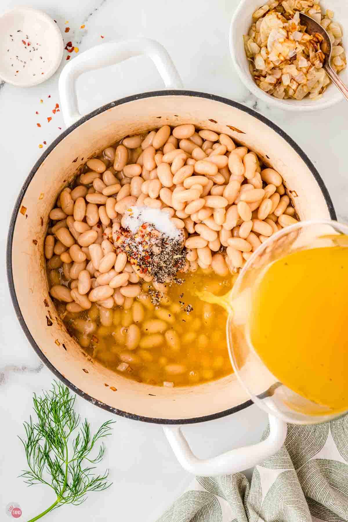white beans in a soup pot with chicken broth being poured in