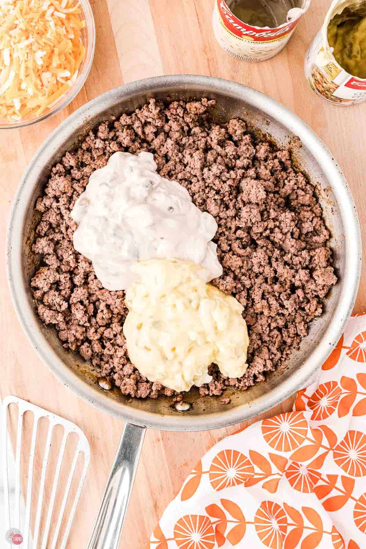 skillet with cooked ground beef and creamy condensed soups on top