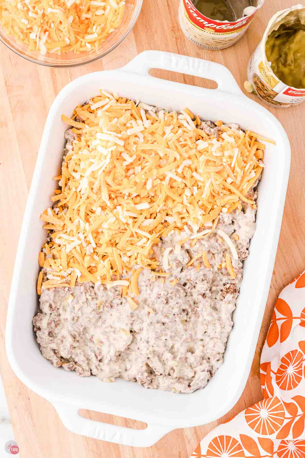 casserole in a white dish being topped with shredded cheese