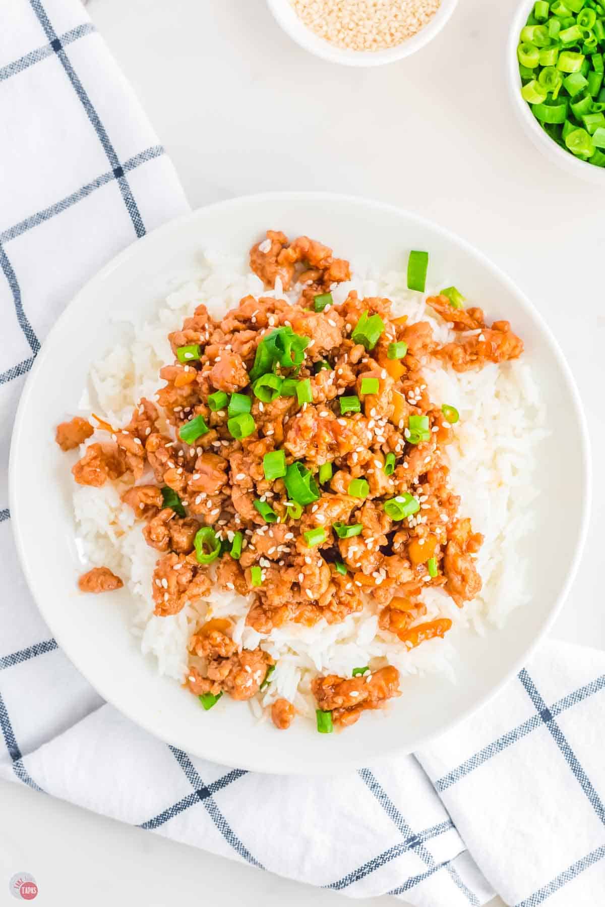 close up of ground orange chicken over white rice on a plate