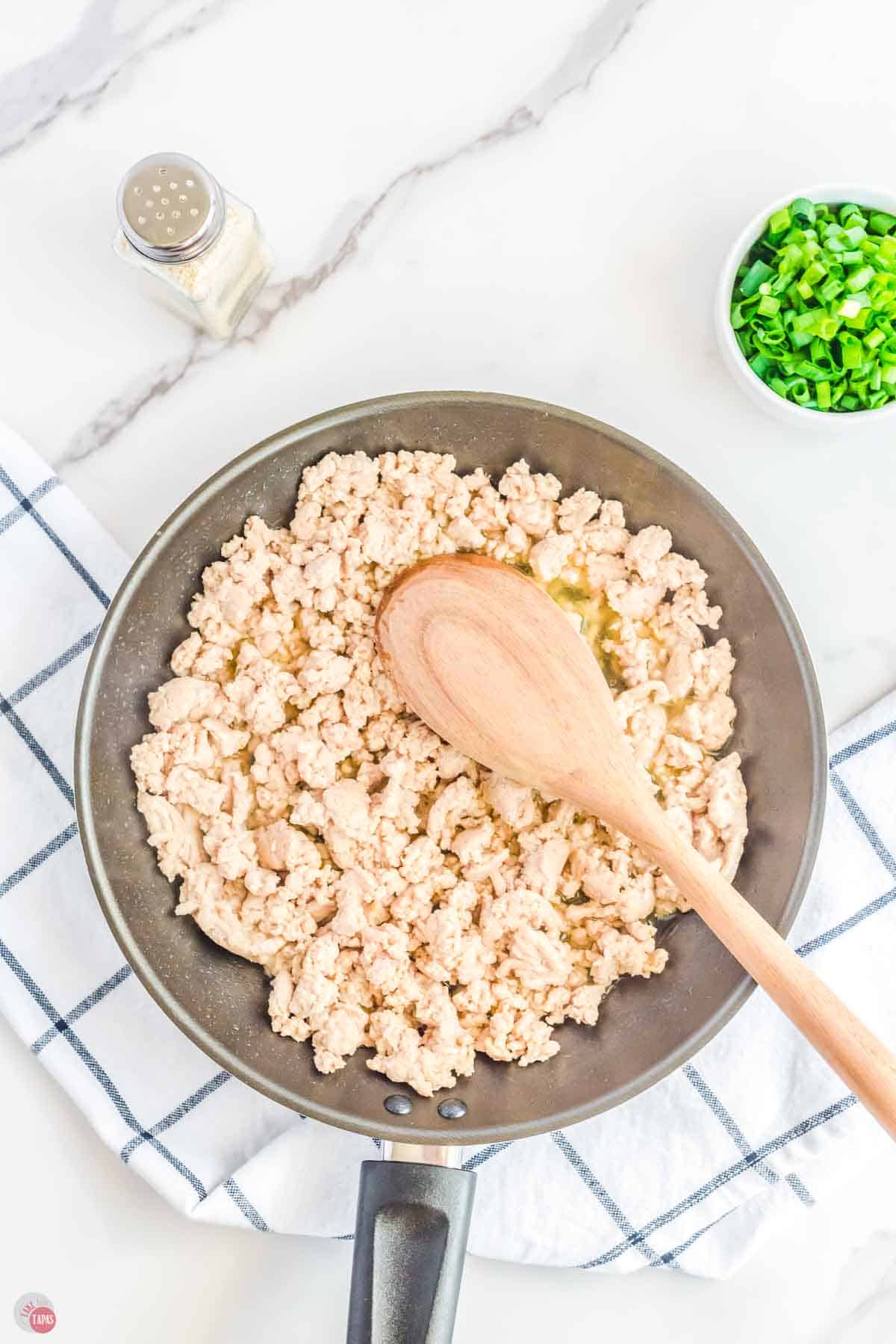 skillet with cooked ground chicken being stirred by a wood spoon