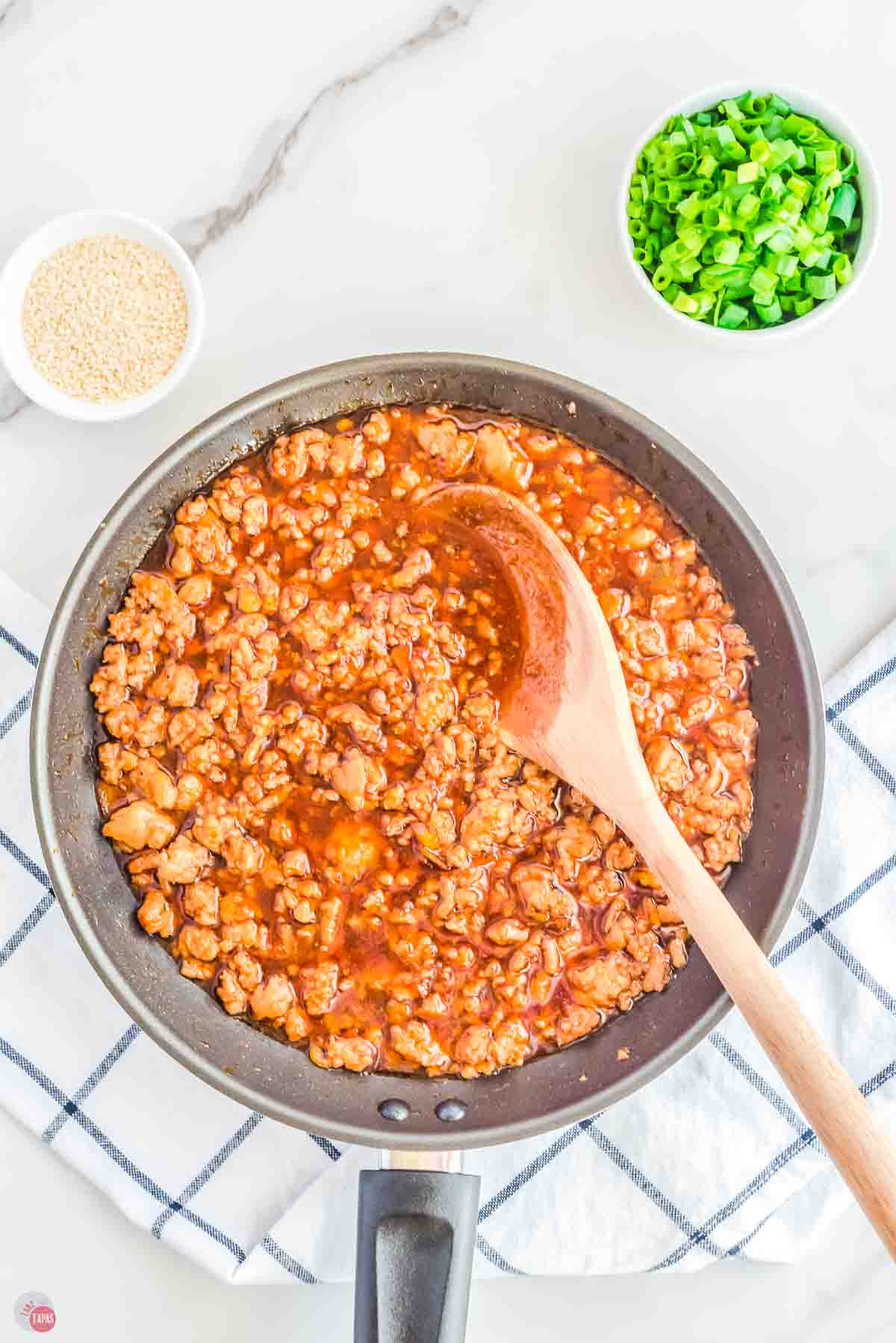 saucy ground orange chicken in a skillet being stirred with a wood spoon
