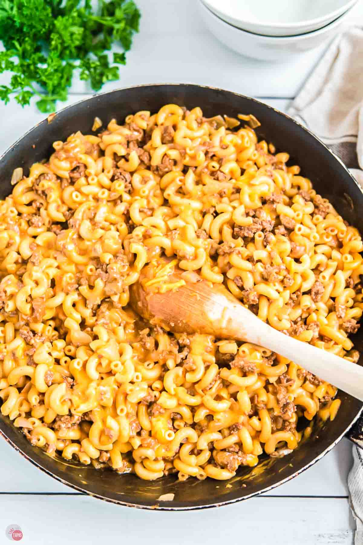 skillet of homemade hamburger helper being stirred with a wood spoon