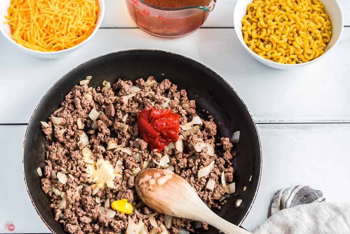 ground beef and onion cooking in a skillet with tomato paste on top