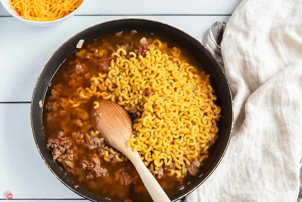 skillet with ground beef, macaroni, and beef broth simmering