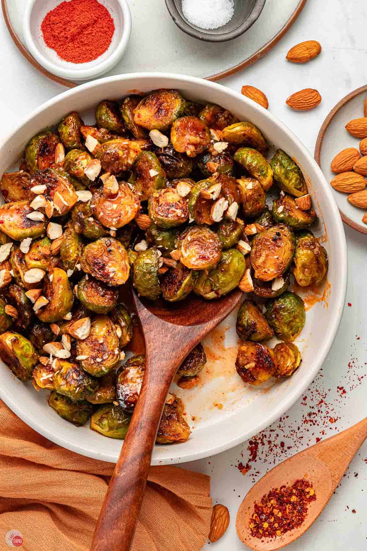 white serving bowl with spicy Brussels sprouts and a large wood spoon