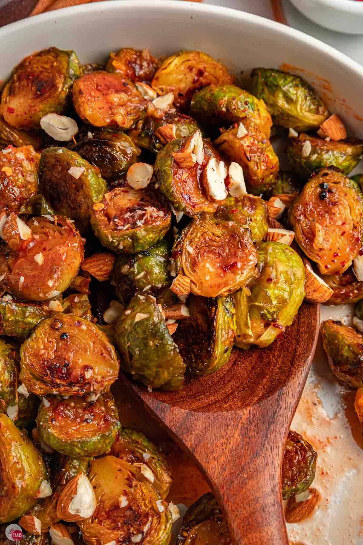 close up of hot honey Brussels sprouts being scooped with a wood spoon