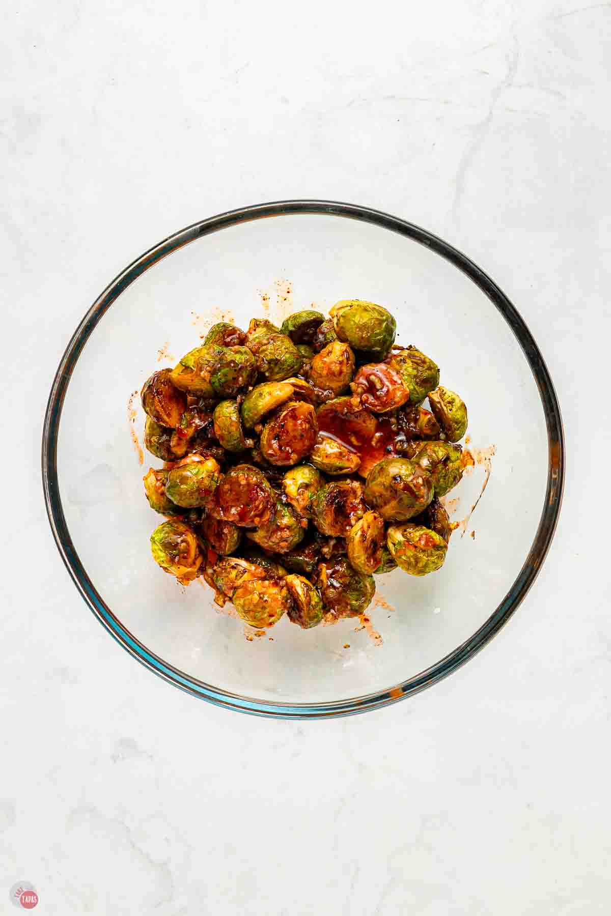 clear mixing bowl filled with Brussels sprouts being tossed in sauce