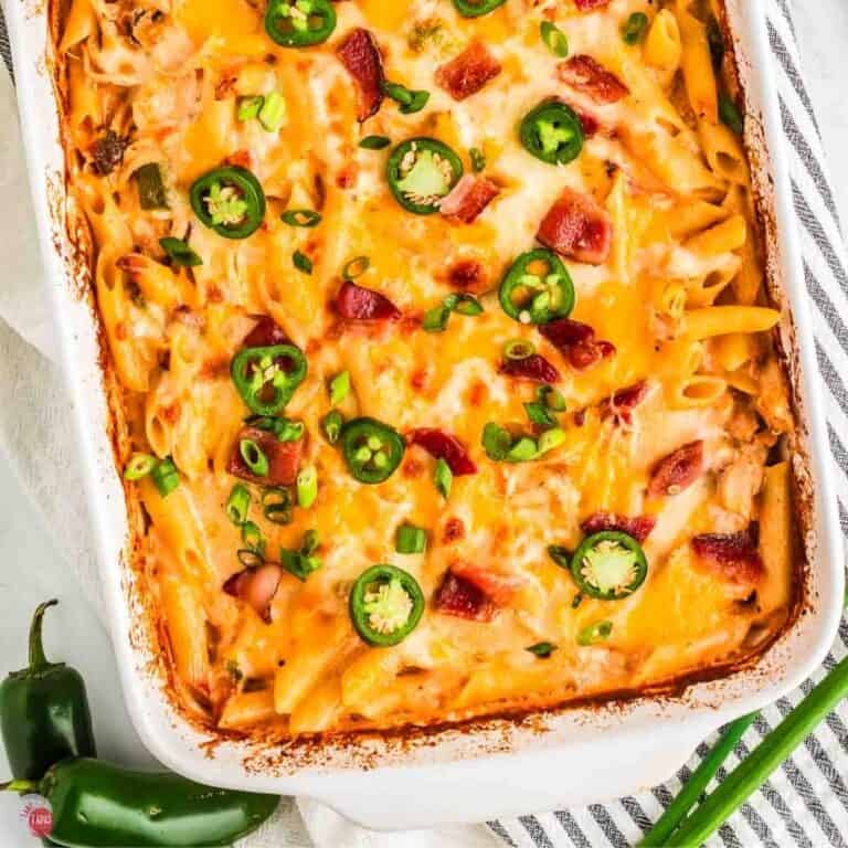 casserole in a white dish with cheese and jalapeno peppers next to a blue and white striped napkin