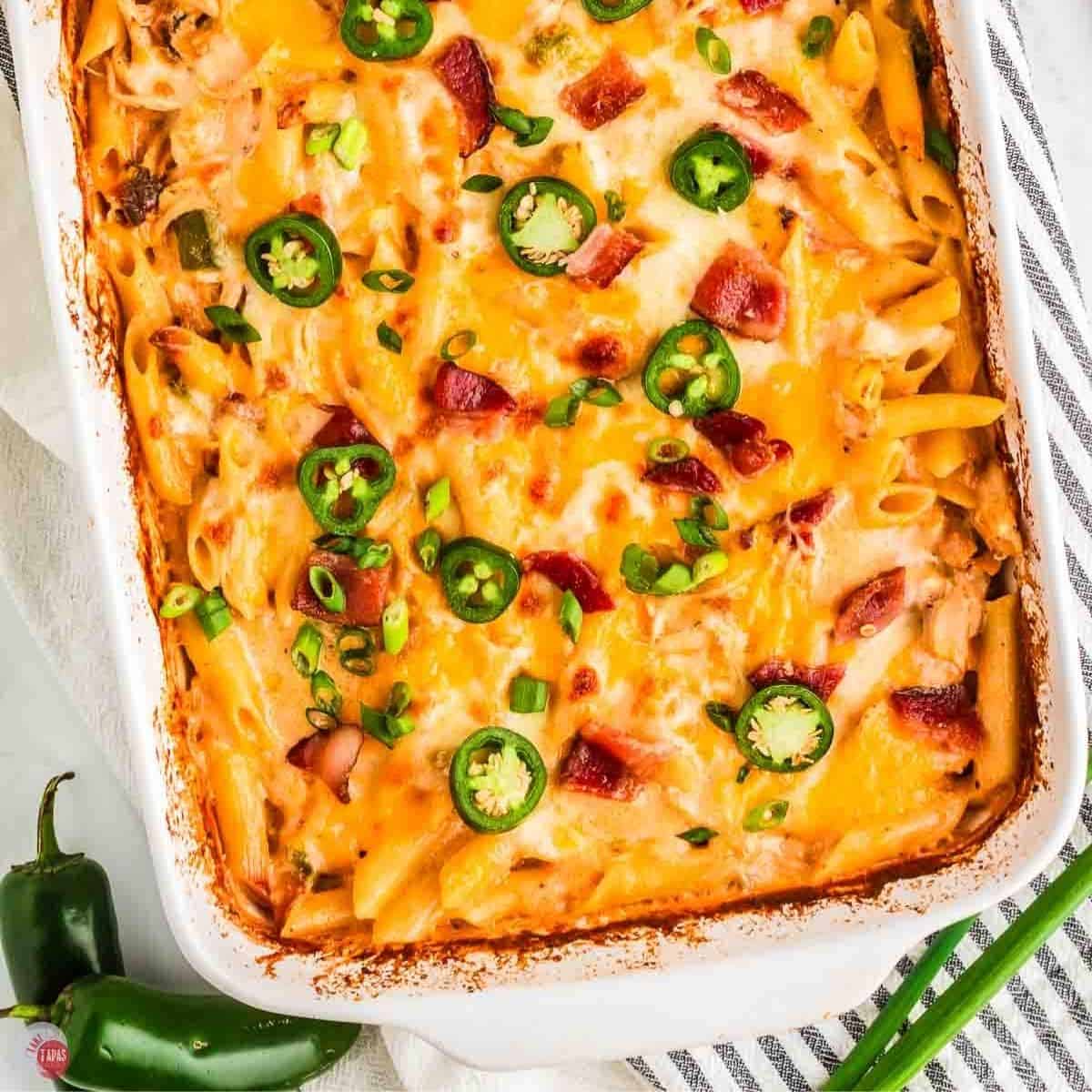 casserole in a white dish with cheese and jalapeno peppers next to a blue and white striped napkin