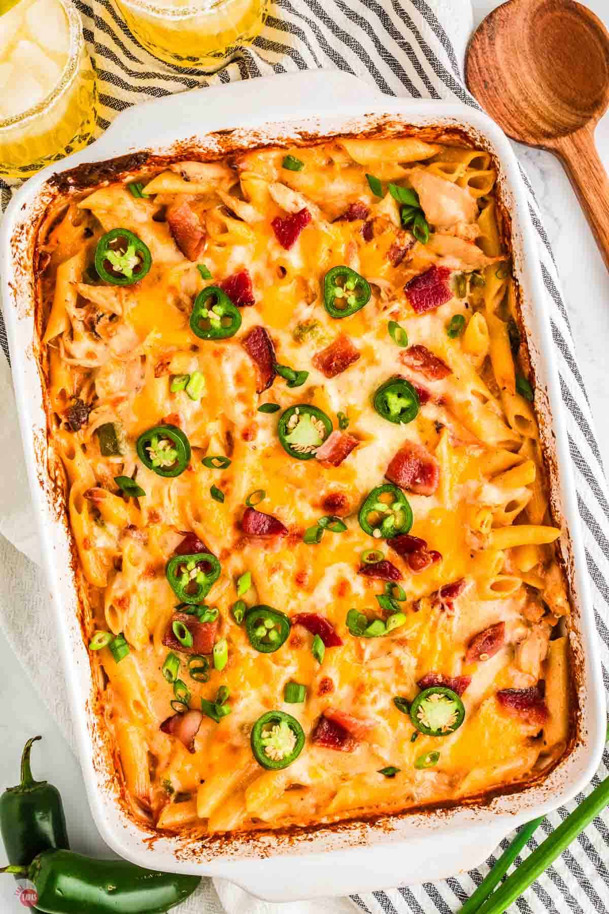 casserole in a white dish with cheese and jalapeno peppers next to a blue and white striped napkin