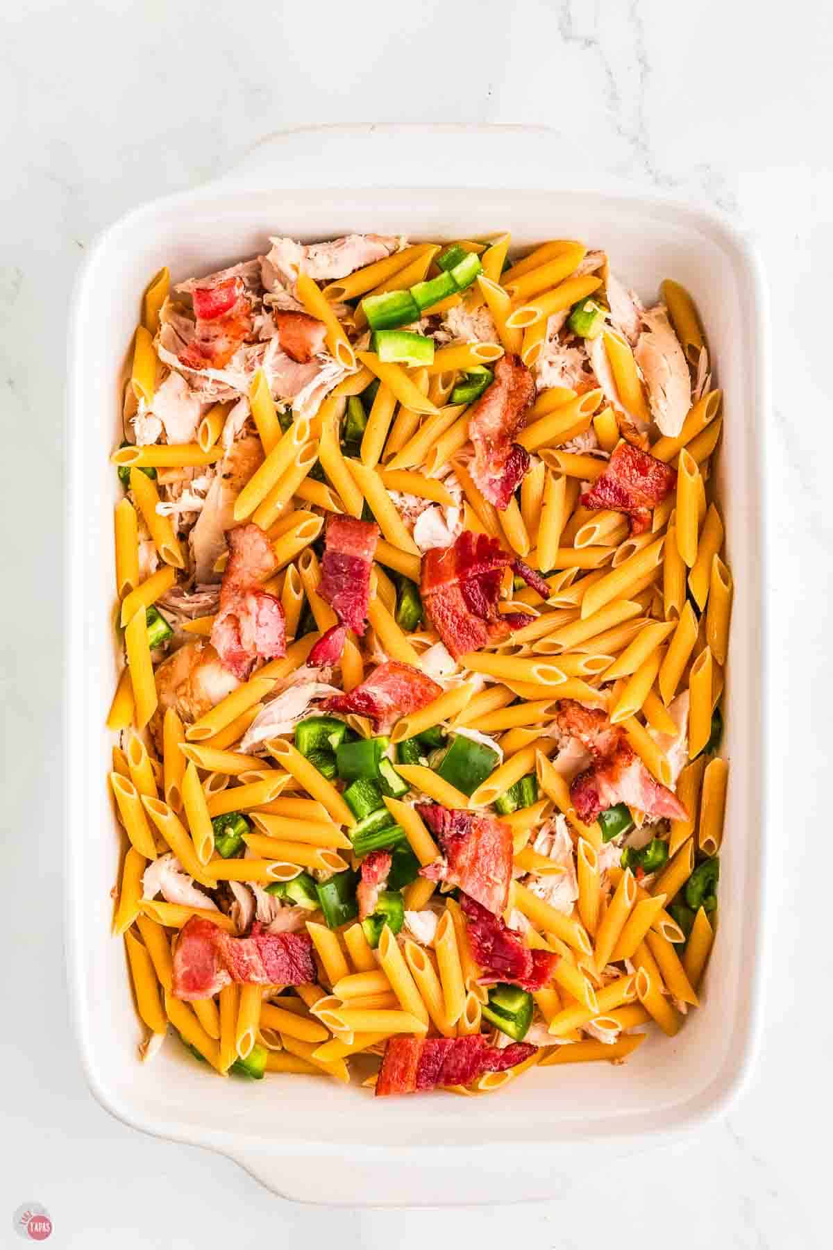 shredded chicken, pasta noodles, bacon, and peppers in a white dish