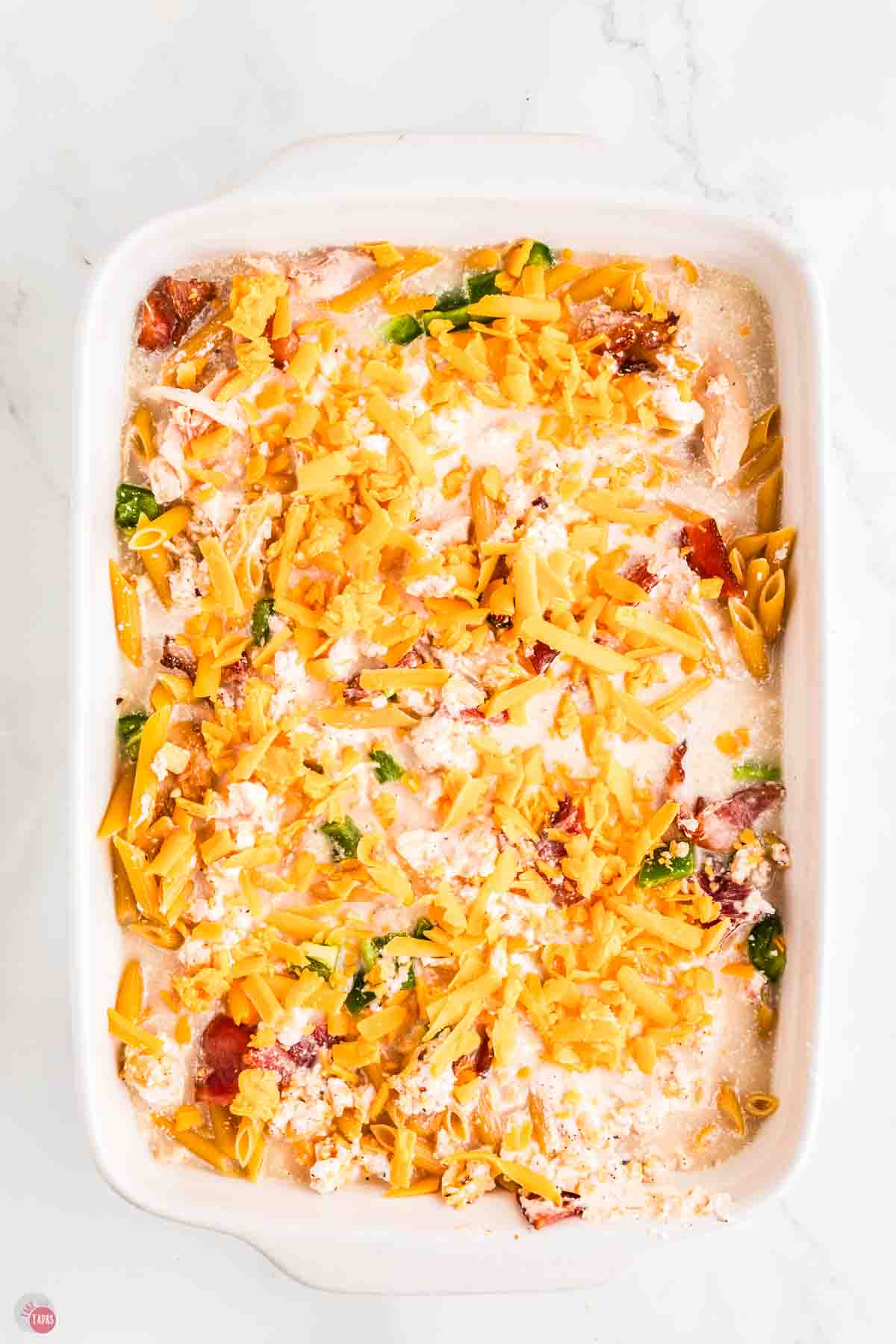 unbaked casserole with pasta, chicken, peppers, and topped with shredded cheese