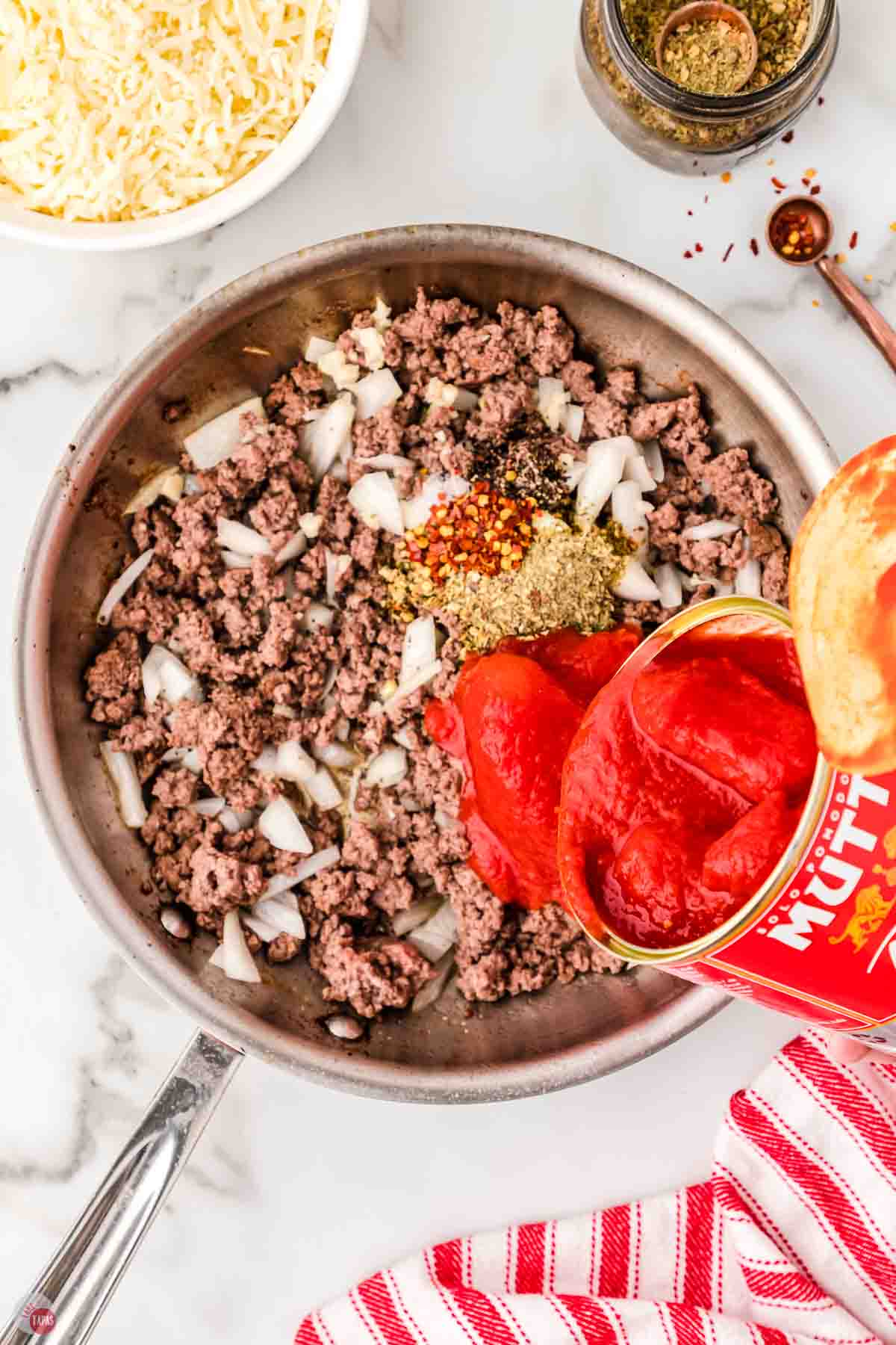 ground beef and onions cooking in a skillet with tomato sauce being poured in