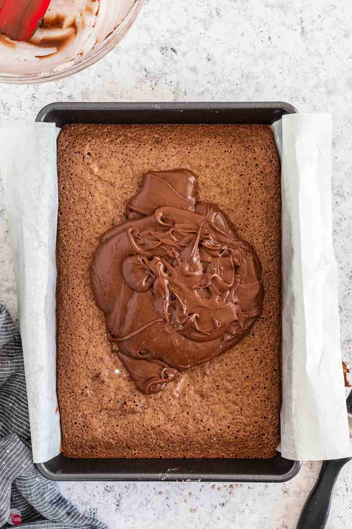 chocolate frosting being poured on baked brownies