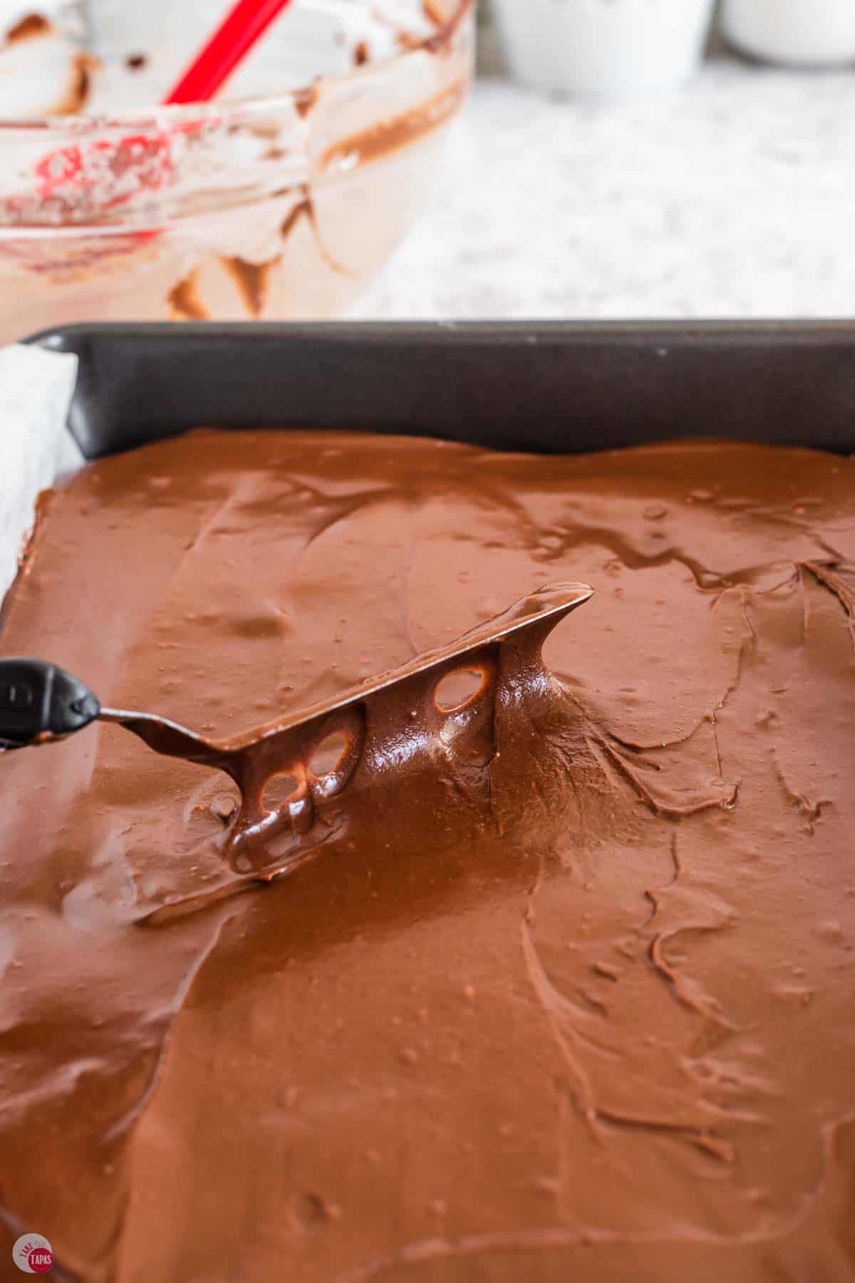 offset spatula spreading melted chocolate frosting over some brownies