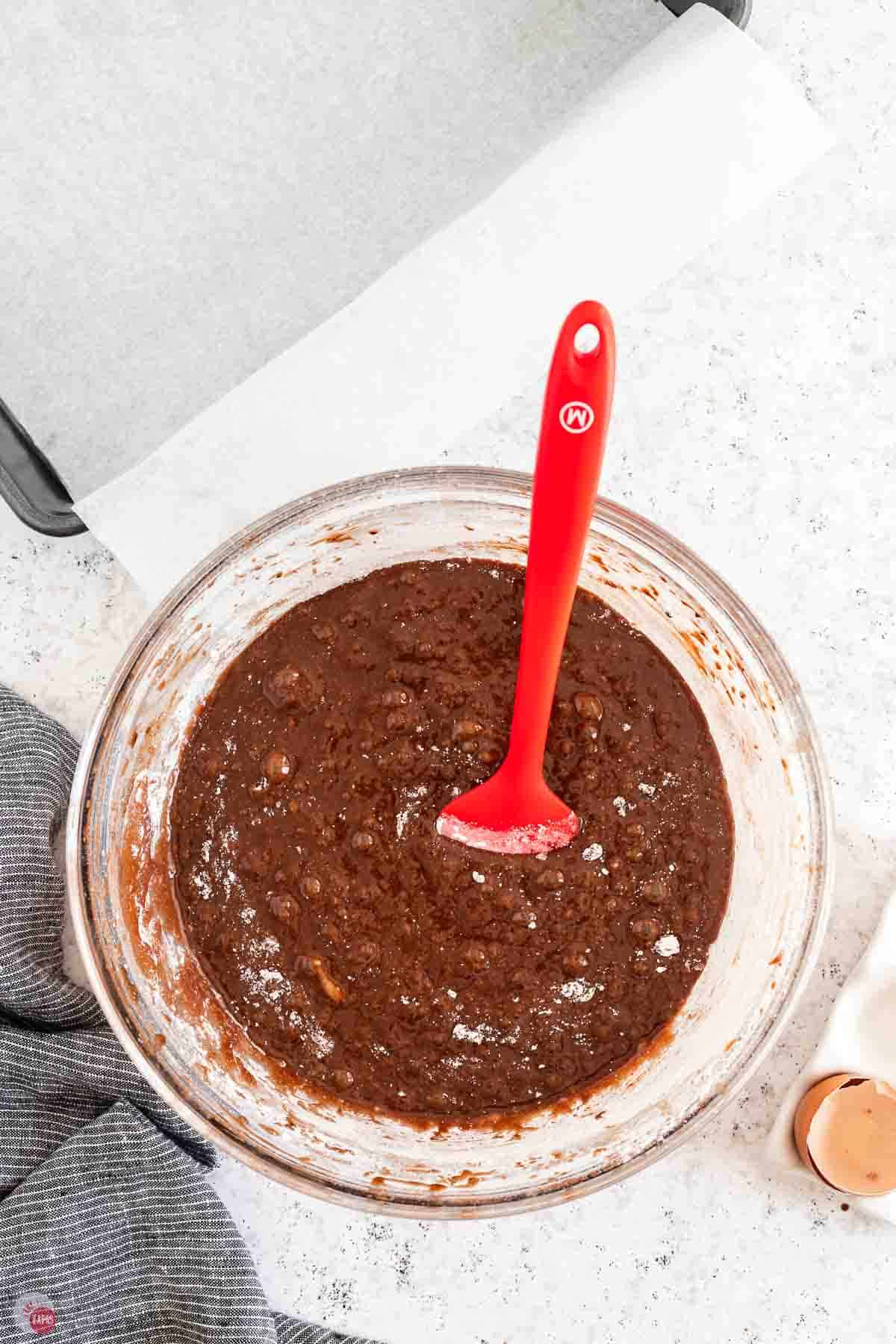 clear bowl of brownie batter with a red spatula