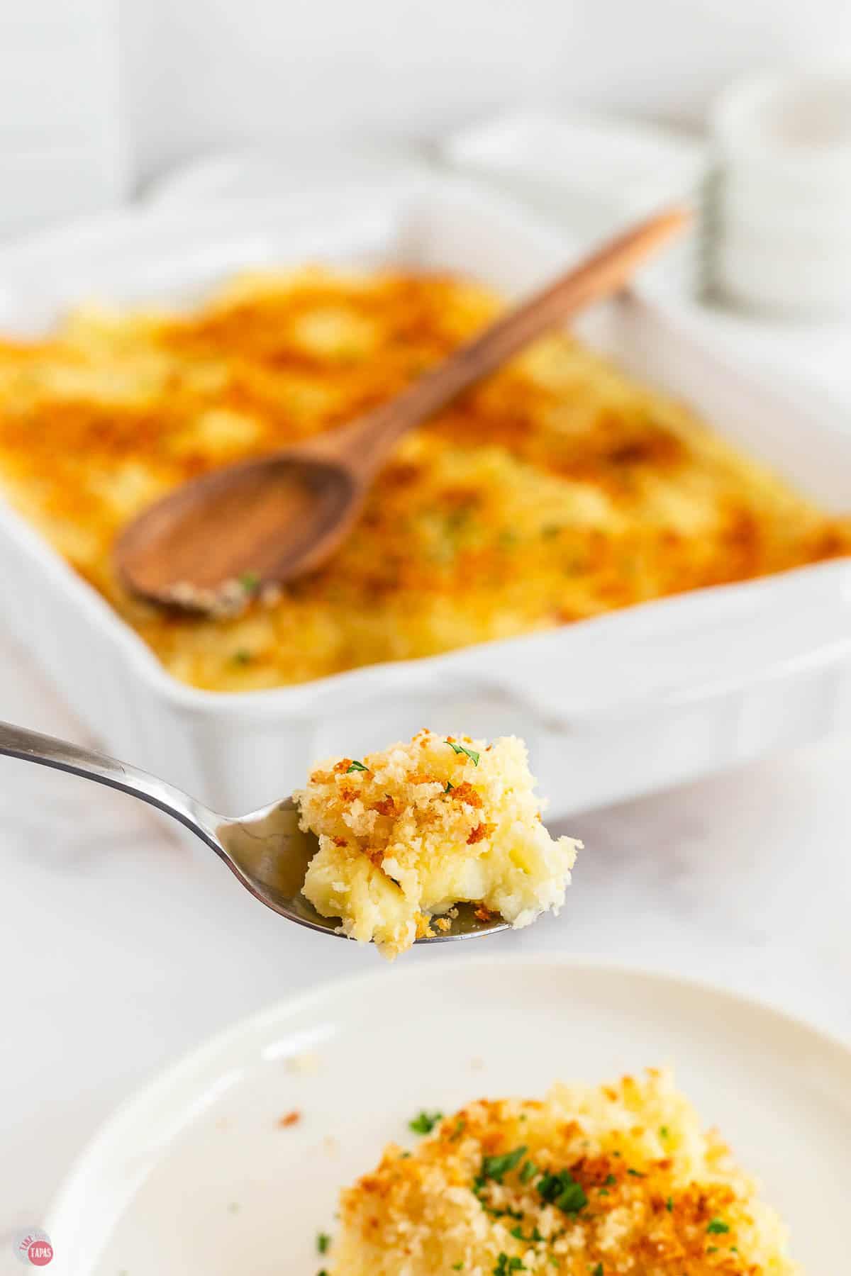 spoon with scoop of mashed potato gratin and a casserole dish behind it