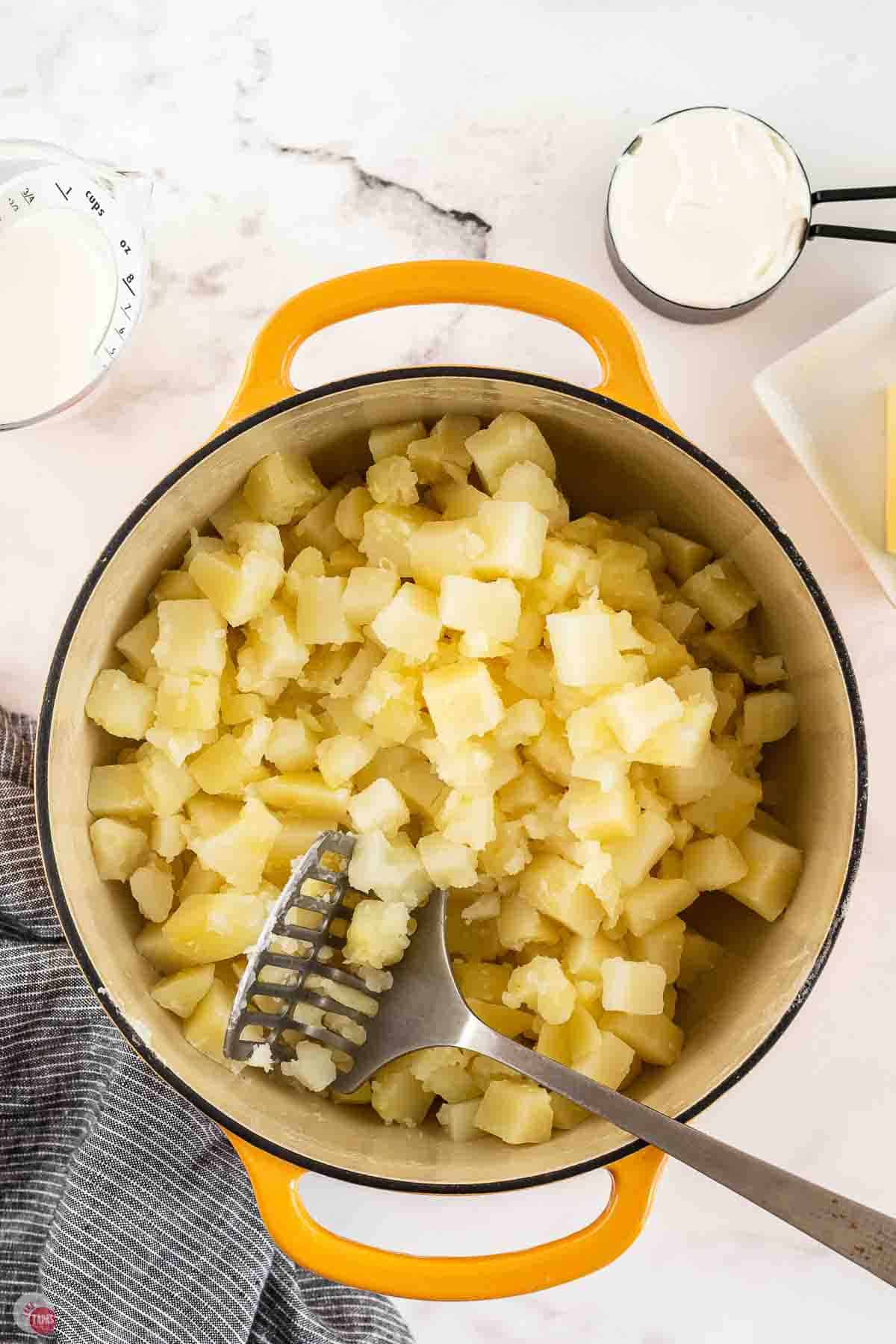 cooked diced potatoes in a large yellow pot with a potato mashed