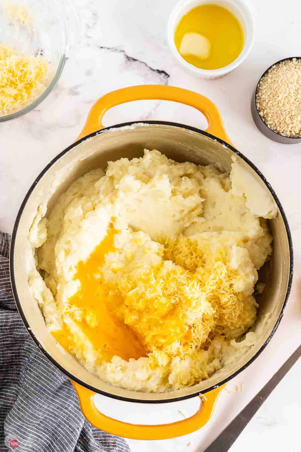 mashed potatoes in a pot with butter, sour cream, and egg being mixed together