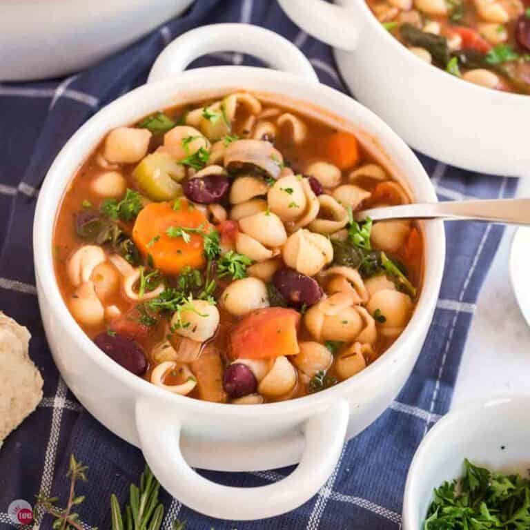 white bowl of minestrone soup with a spoon and a blue napkin