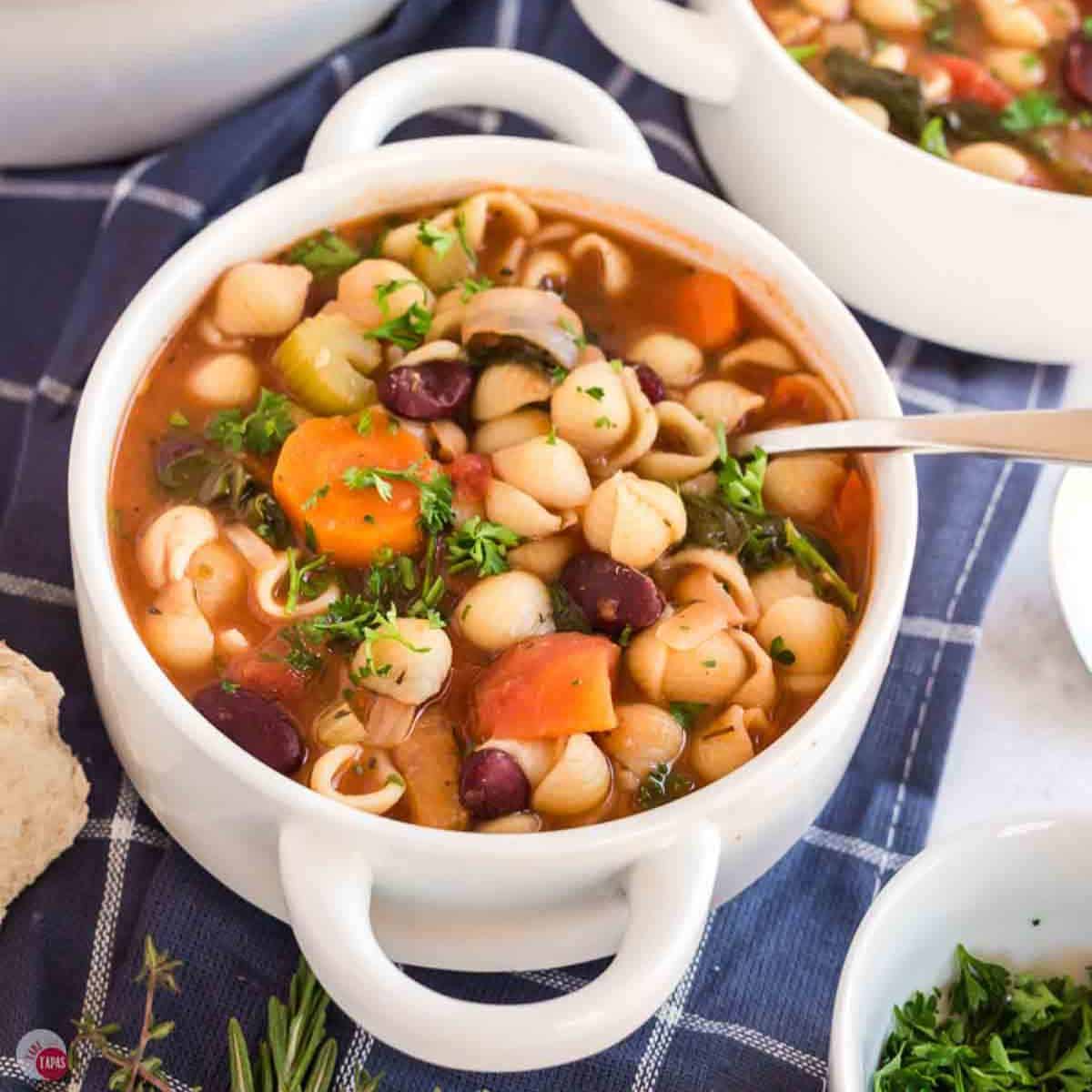 white bowl of minestrone soup with a spoon and a blue napkin