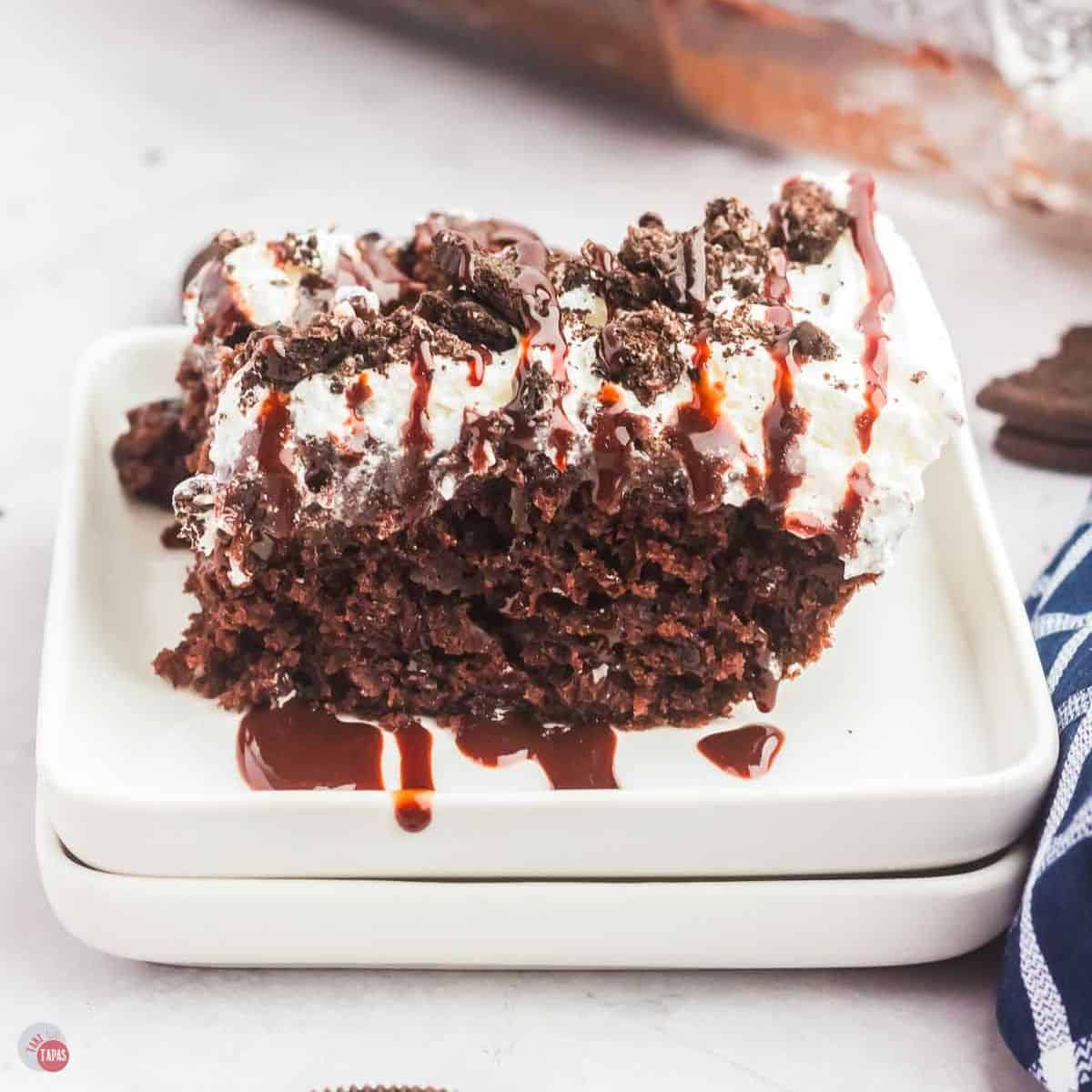 slice of chocolate cake with crushed Oreo cookies on a stack of white plates