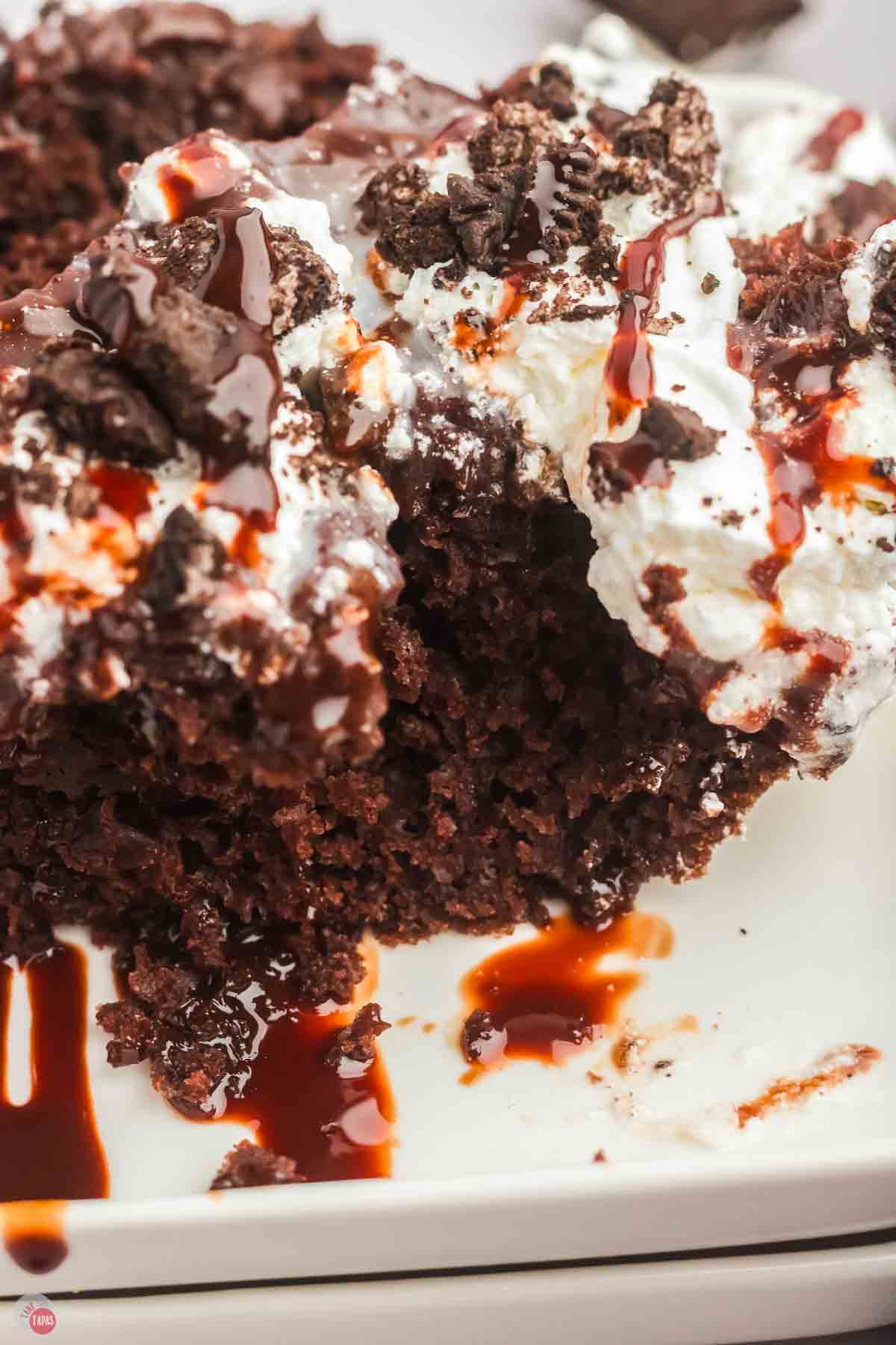 close up of chocolate cake topped with whipped cream, crushed cookies, and chocolate sauce