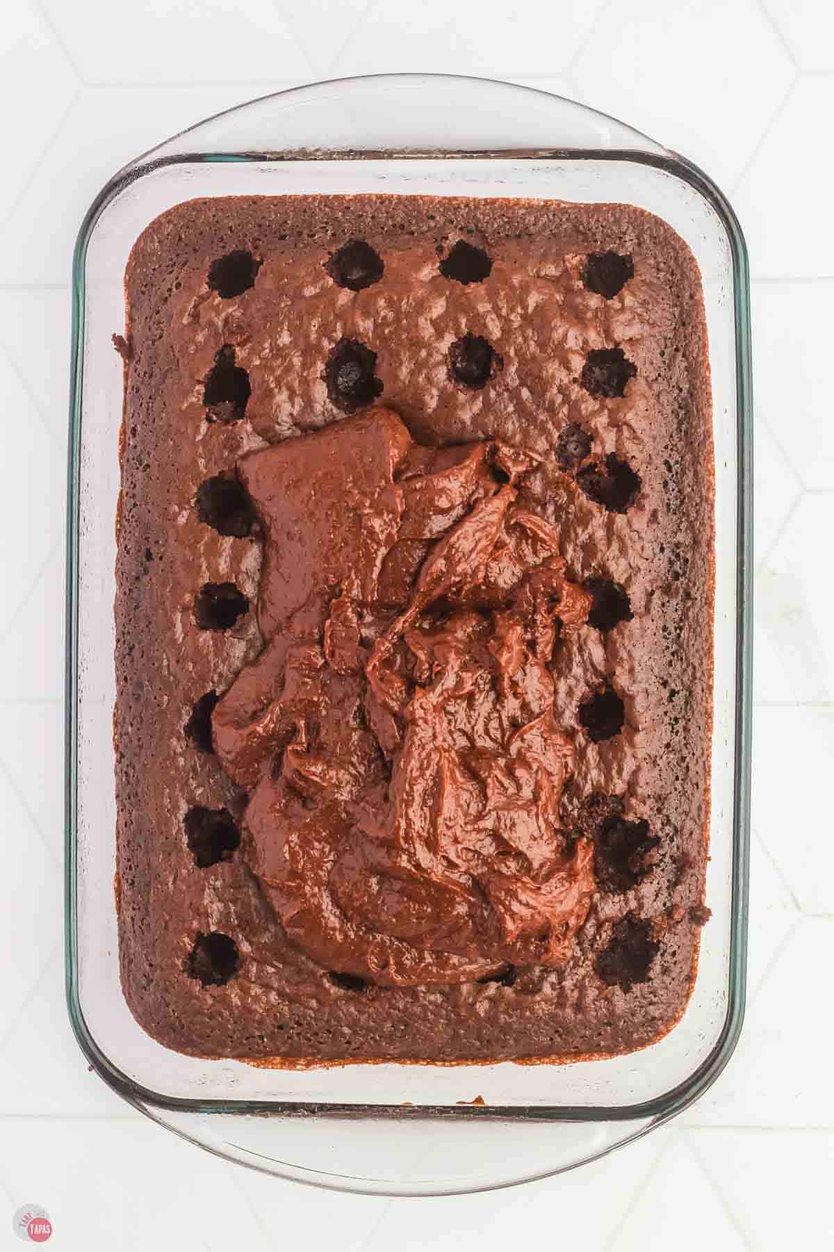 baked chocolate cake in a dish with holes poked it in and a pile of frosting on top