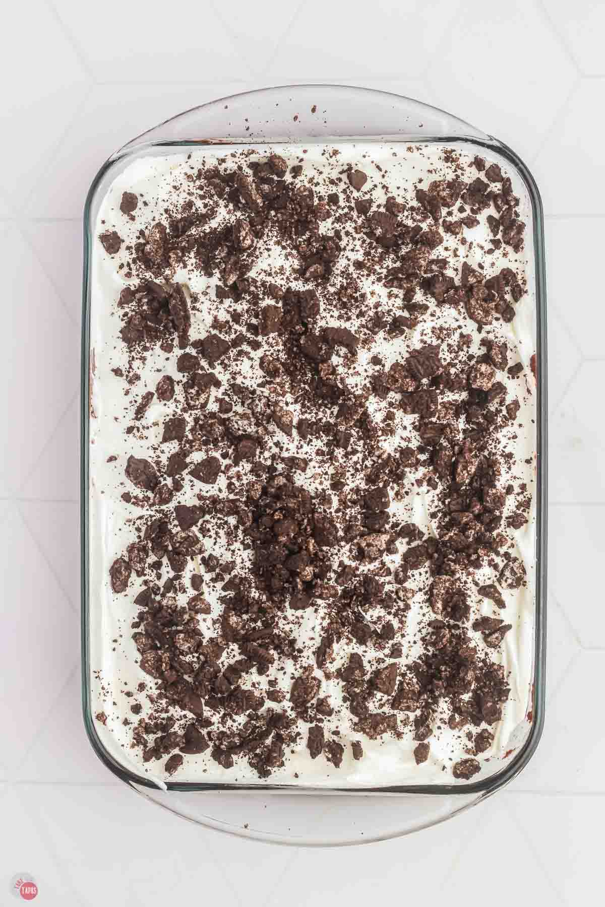 oreo poke cake in a baking dish topped with whipped cream and crushed Oreo cookies