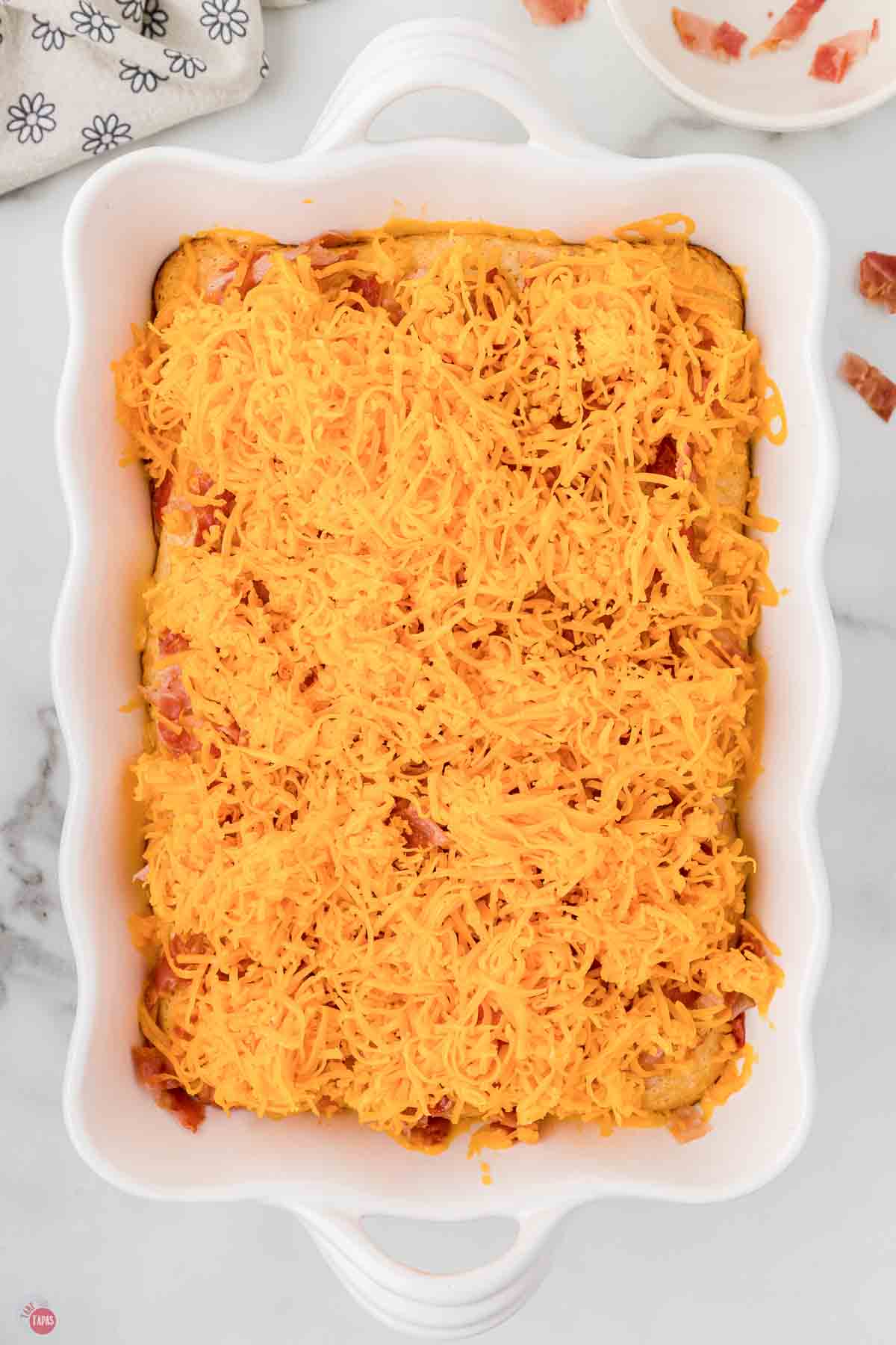 white casserole dish with bacon pieces and shredded cheese