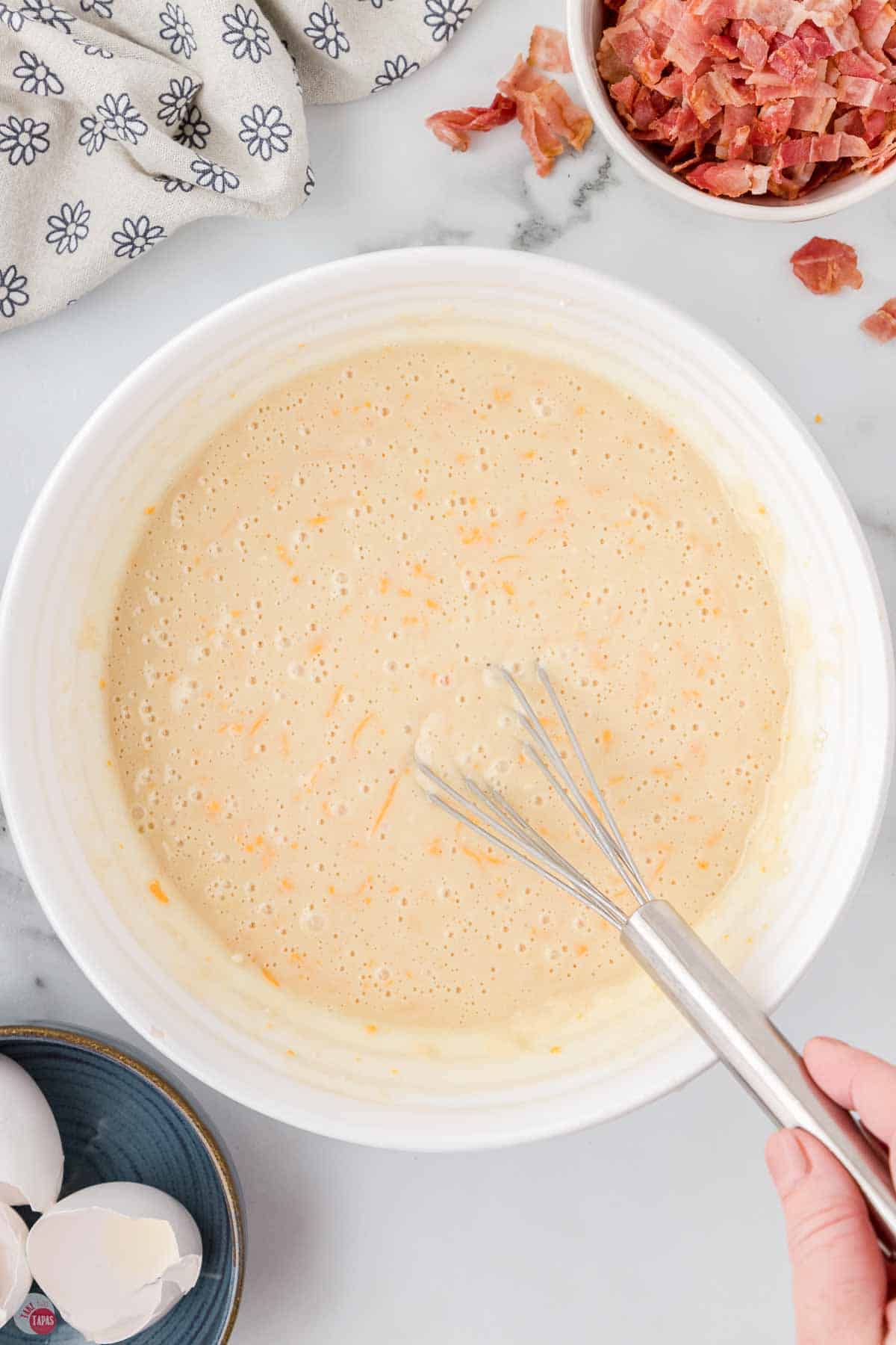 pancake batter mixed with cheese in a white bowl with a whisk