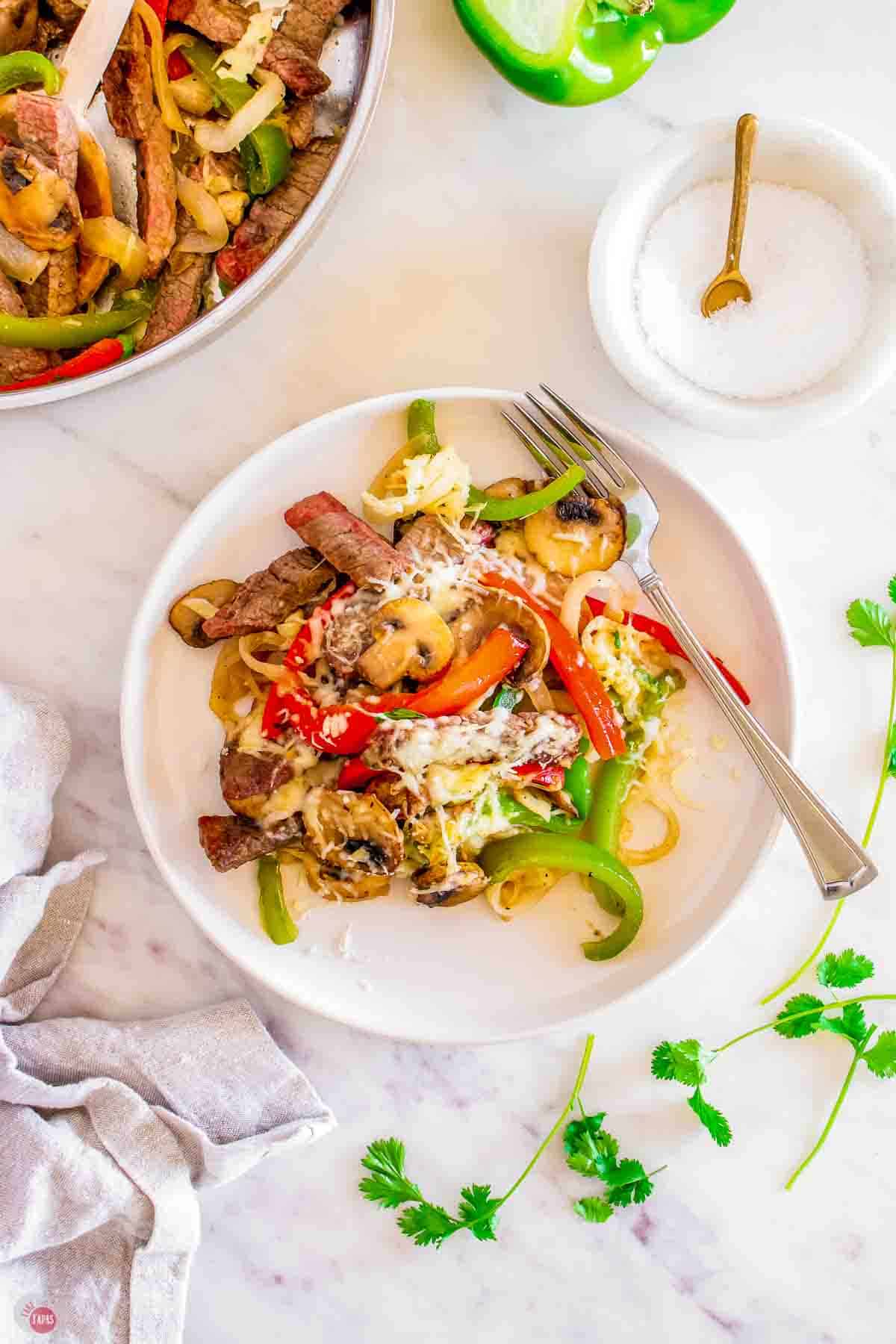 plate with seared steak, bell peppers, onions, and mushrooms topped with melted cheese.