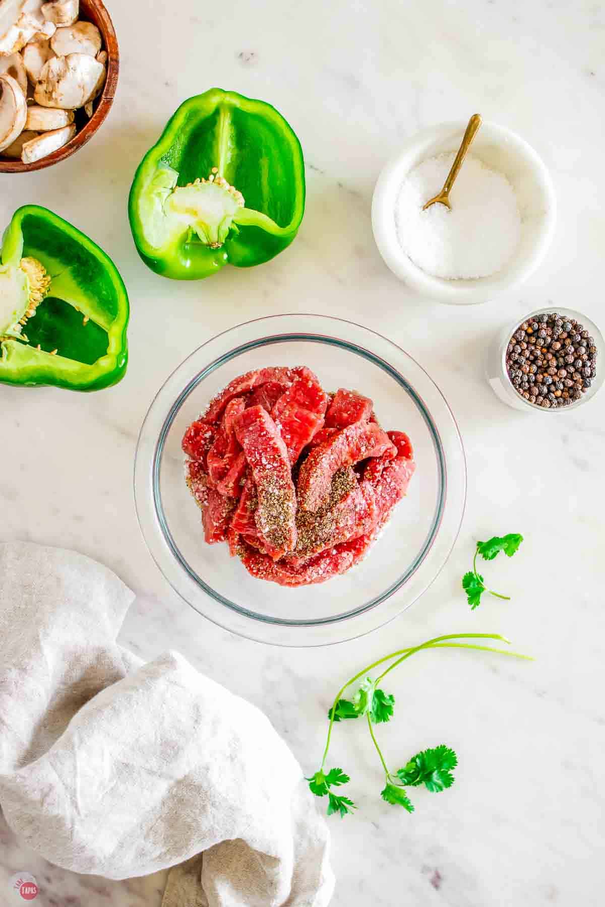 sliced steak in a clear mixing bowl topped with salt and pepper