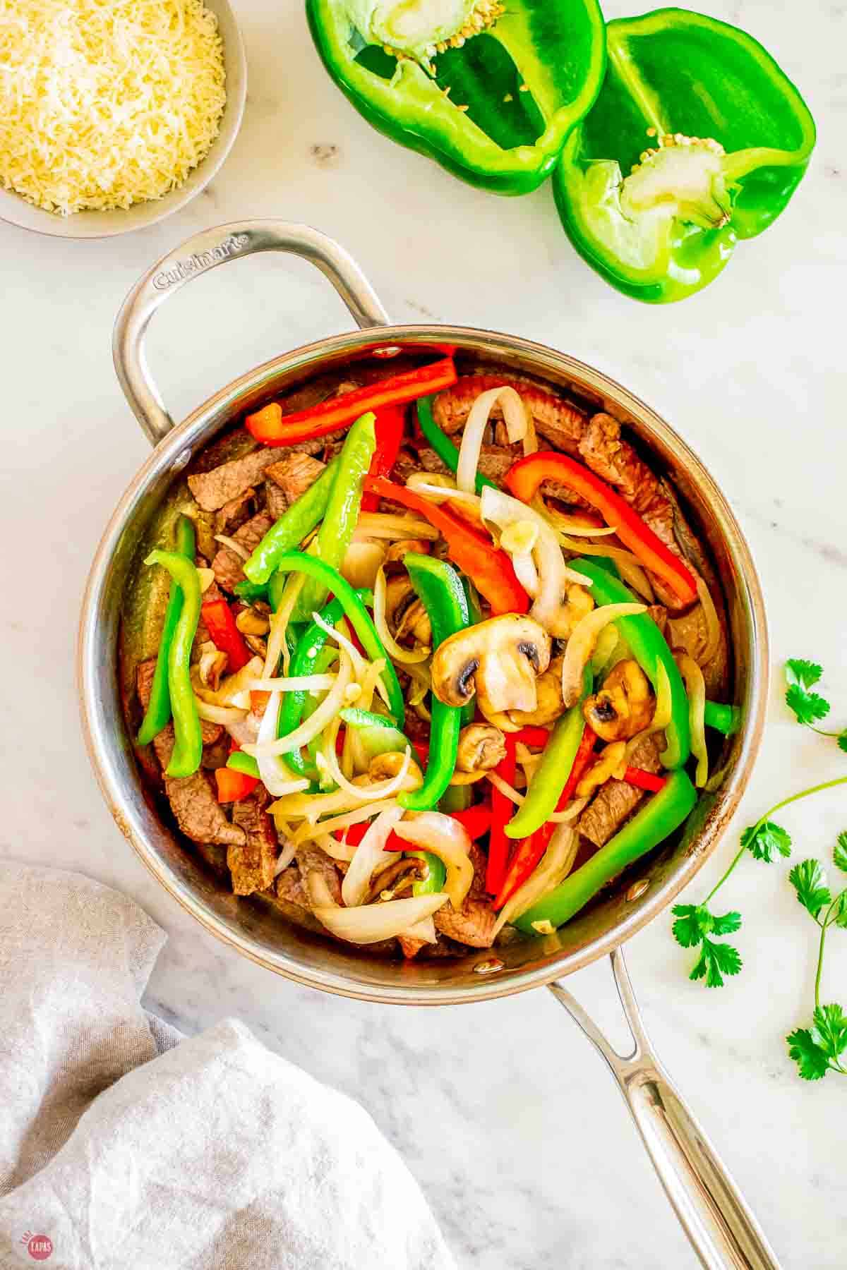philly steak cooking in a skillet with peppers and onions