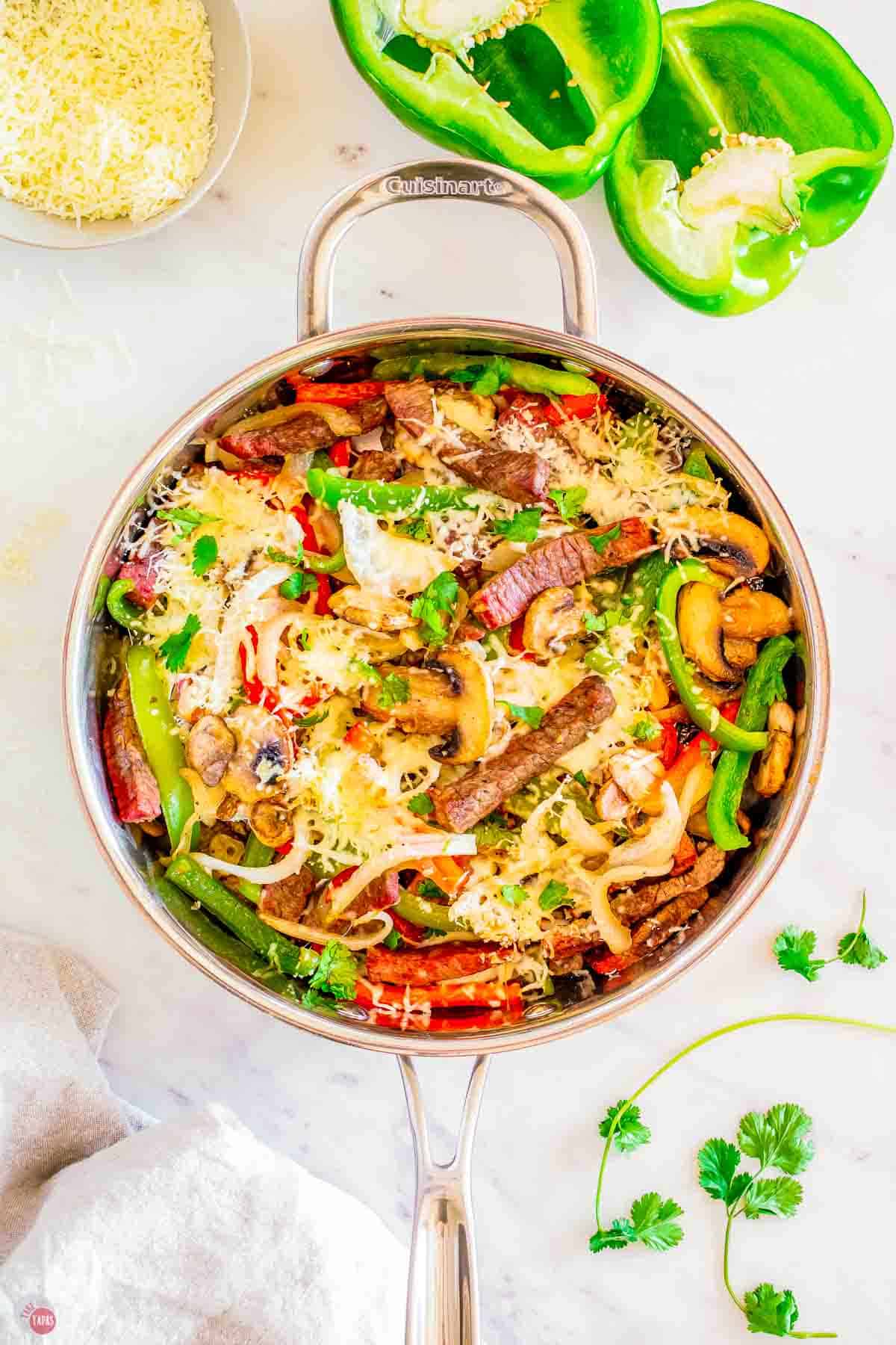 skillet with steak, peppers, and onions cooking