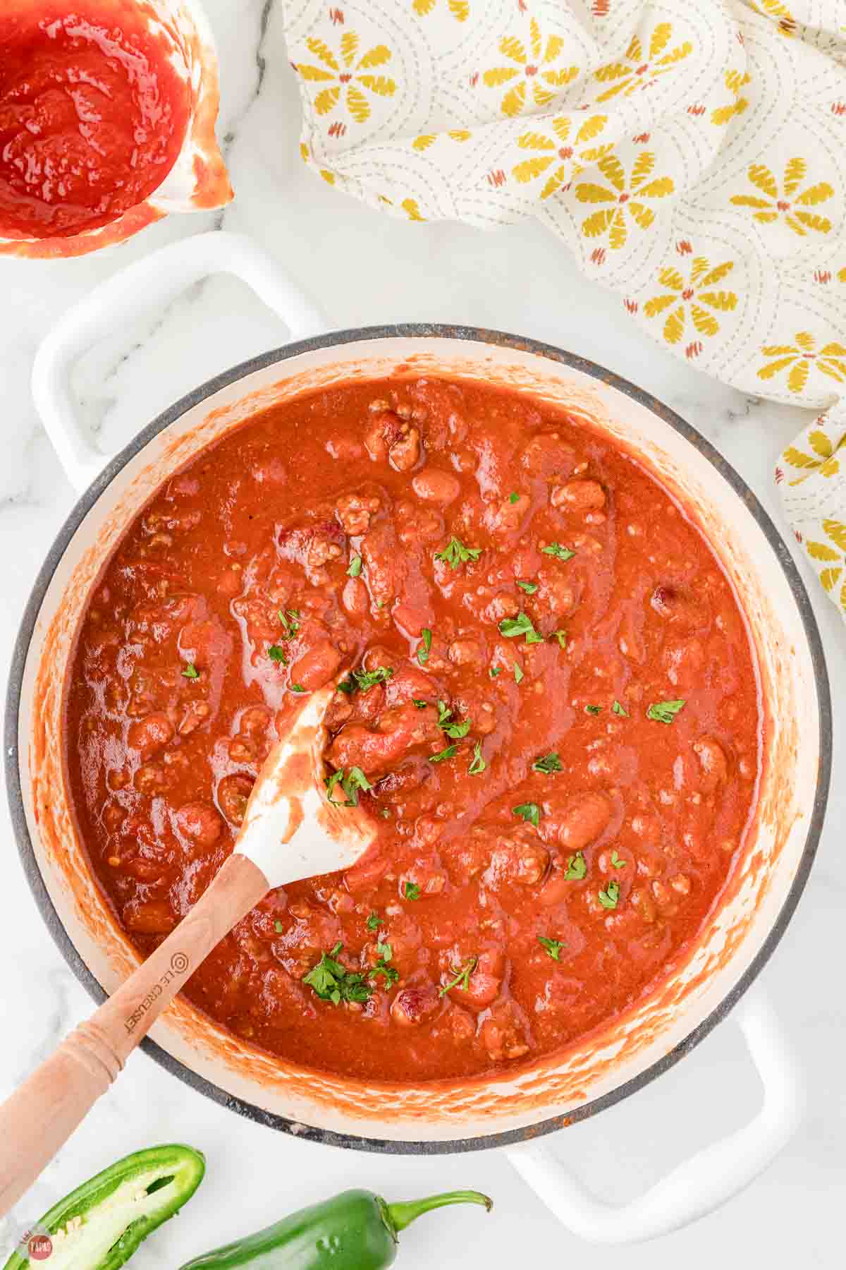 white soup pot with chili being stirred with a white spatula