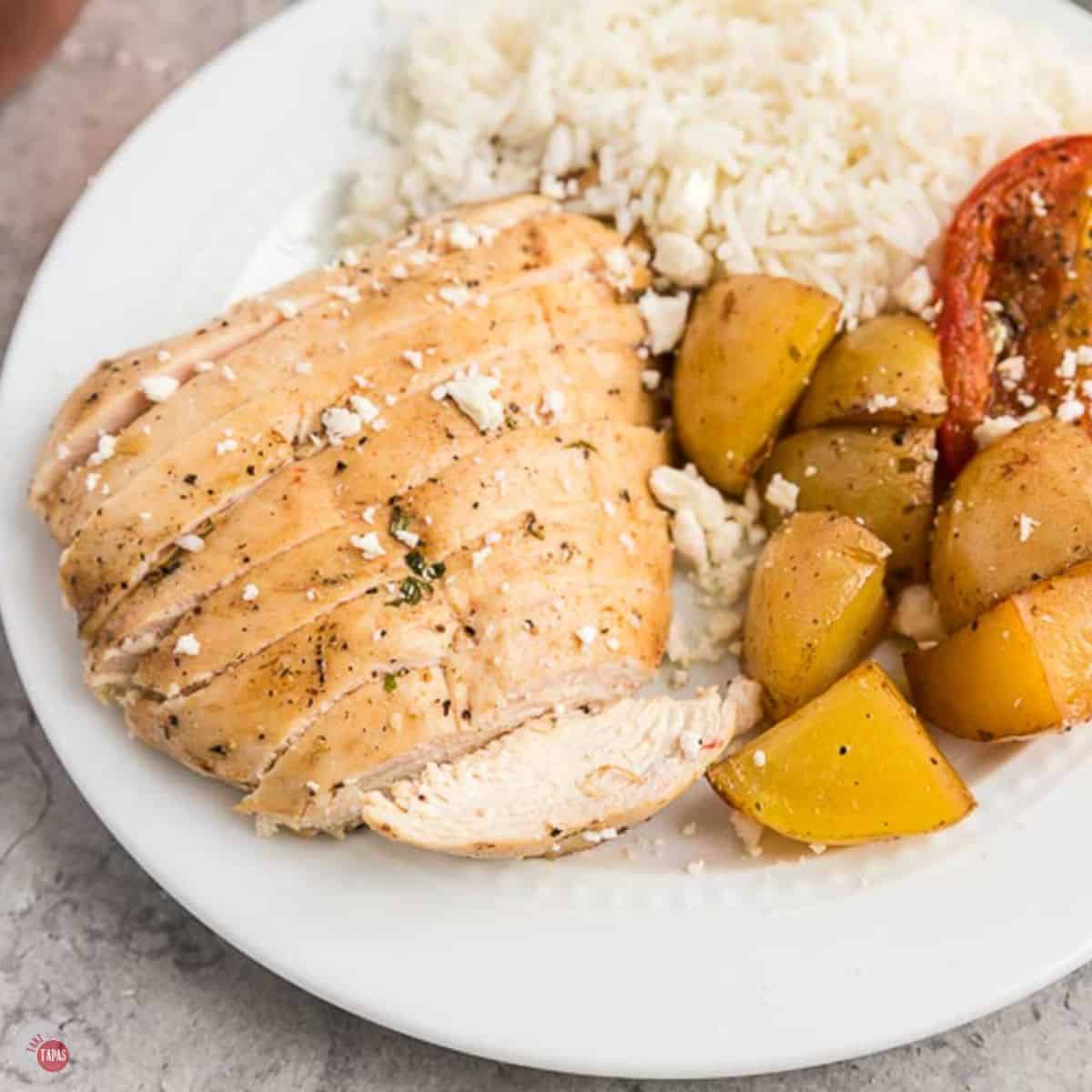 sliced chicken, rice, potatoes, and tomatoes on a white plate