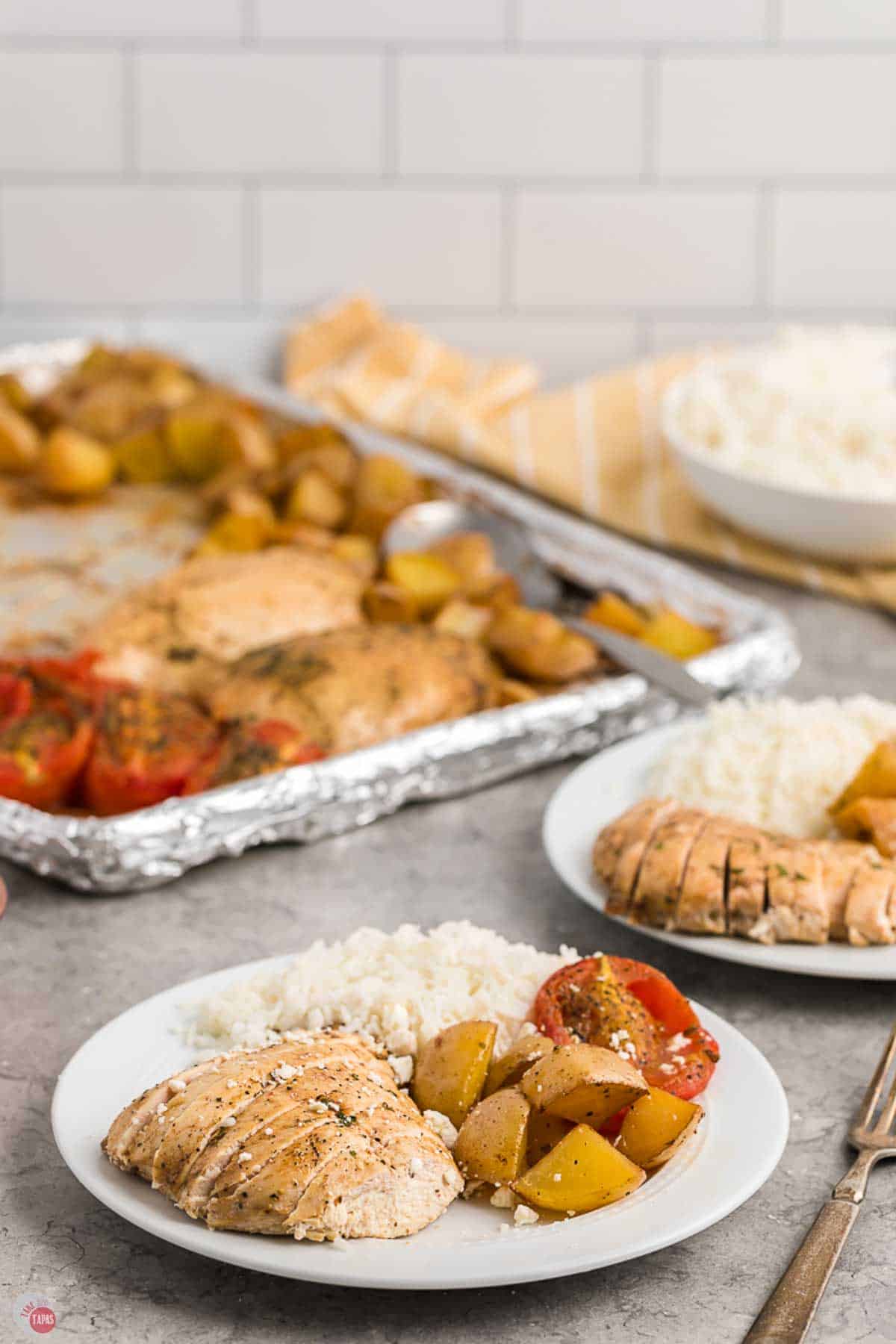 plate of chicken, tomatoes, and potatoes in front of a sheet pan