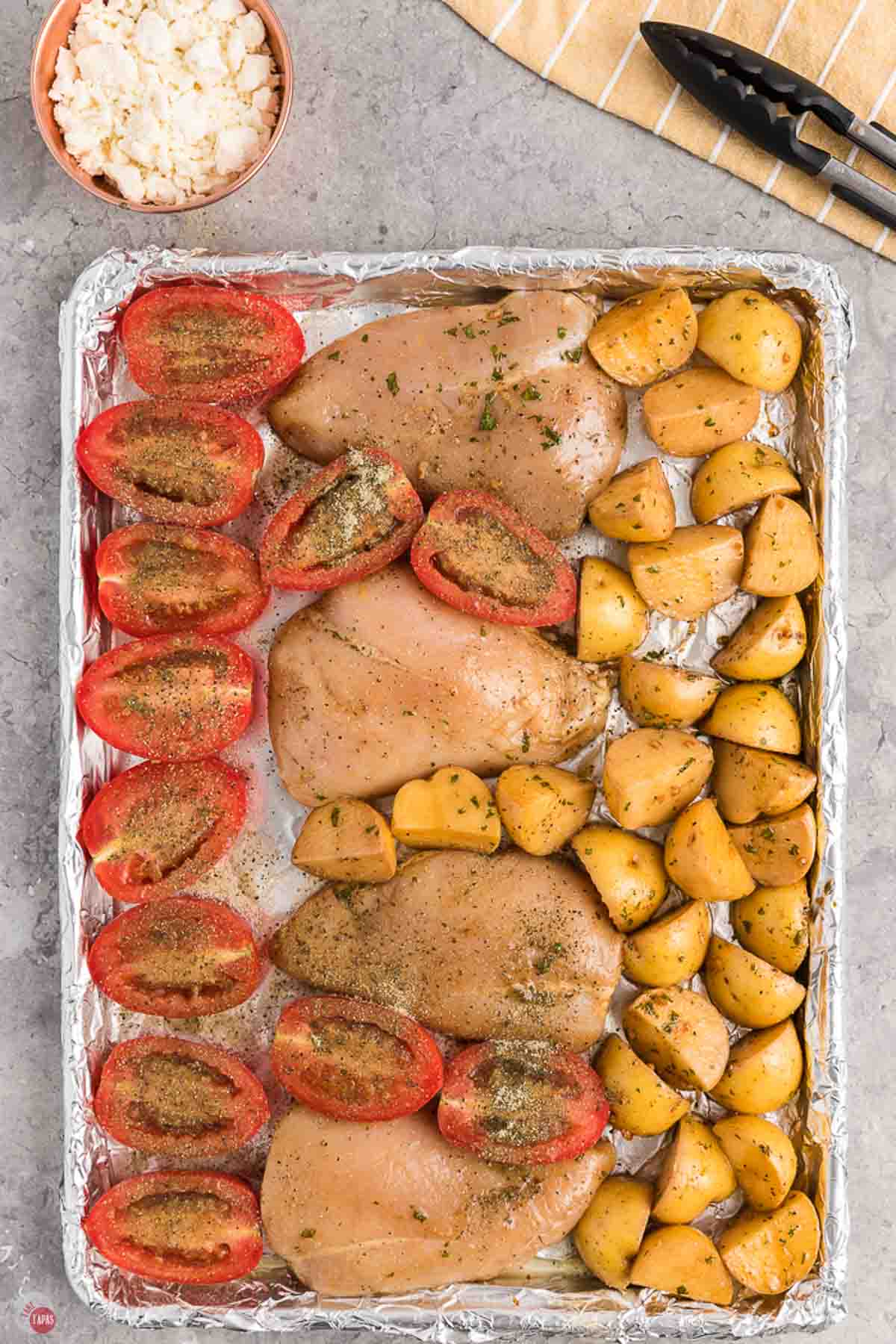 chicken, tomatoes, and potatoes on a baking sheet