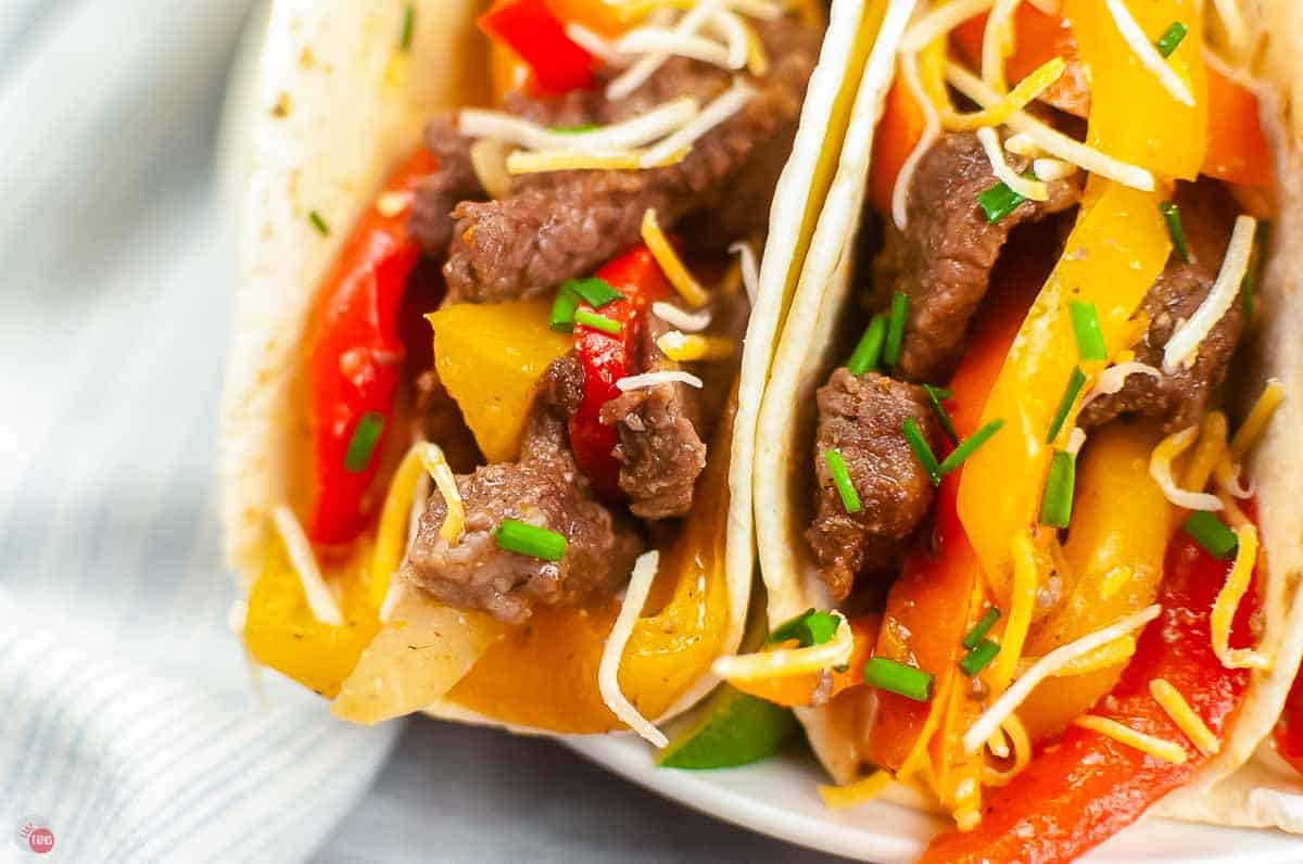 close up of steak fajita meat and vegetables stuffed into flour tortillas