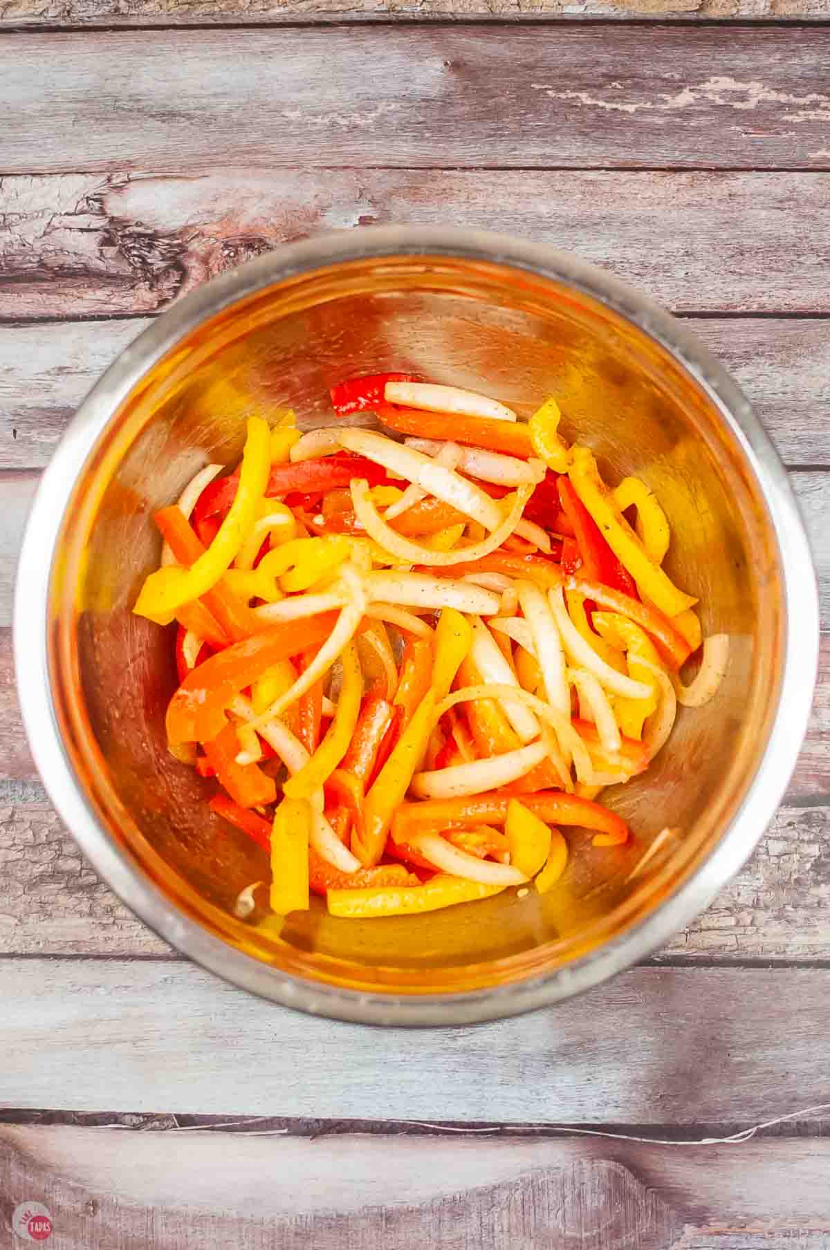 sliced bell peppers and onions in a metal mixing bowl with seasoning