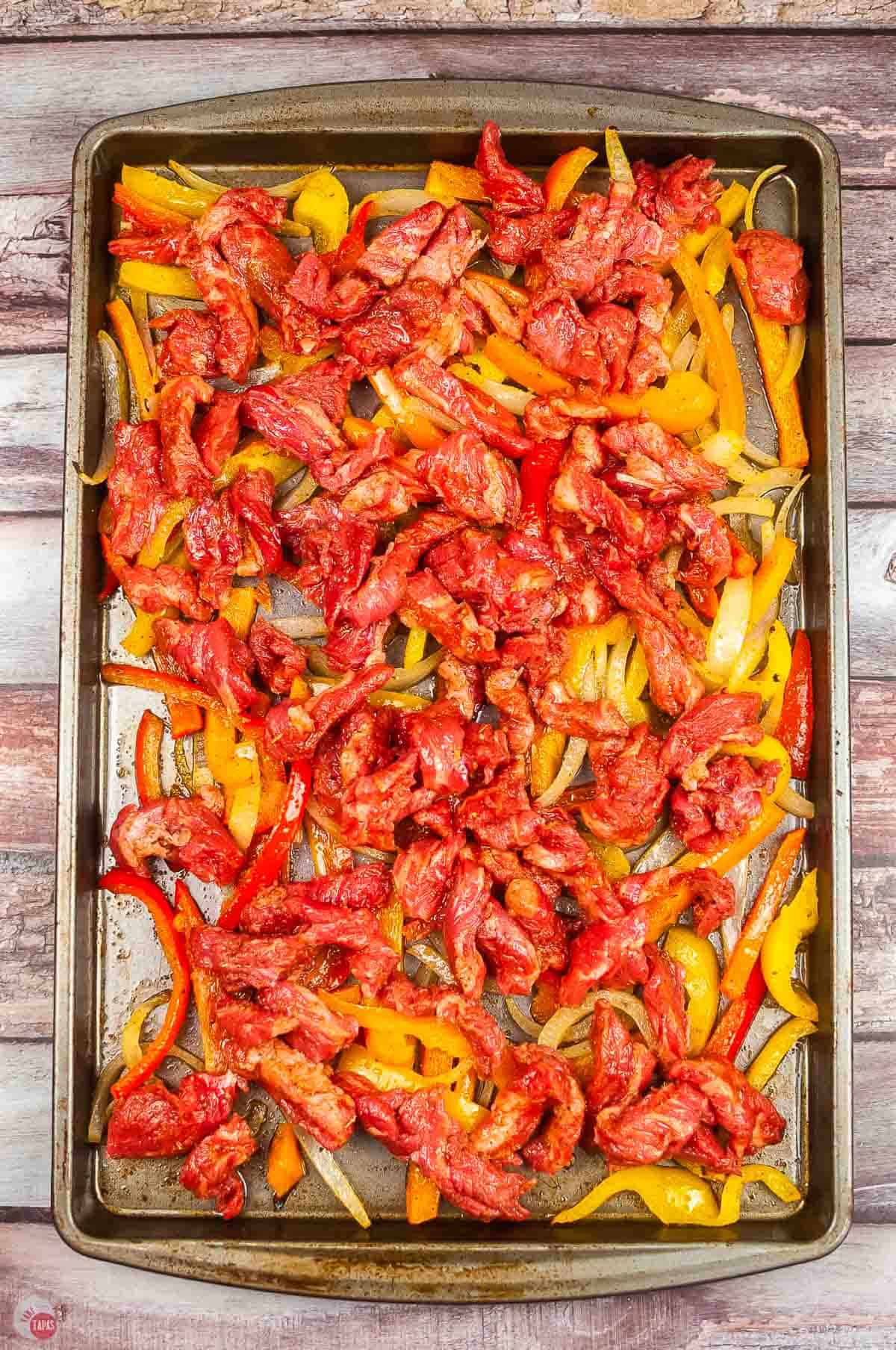 sheet pan topped with bell peppers, onions, and sliced flank steak