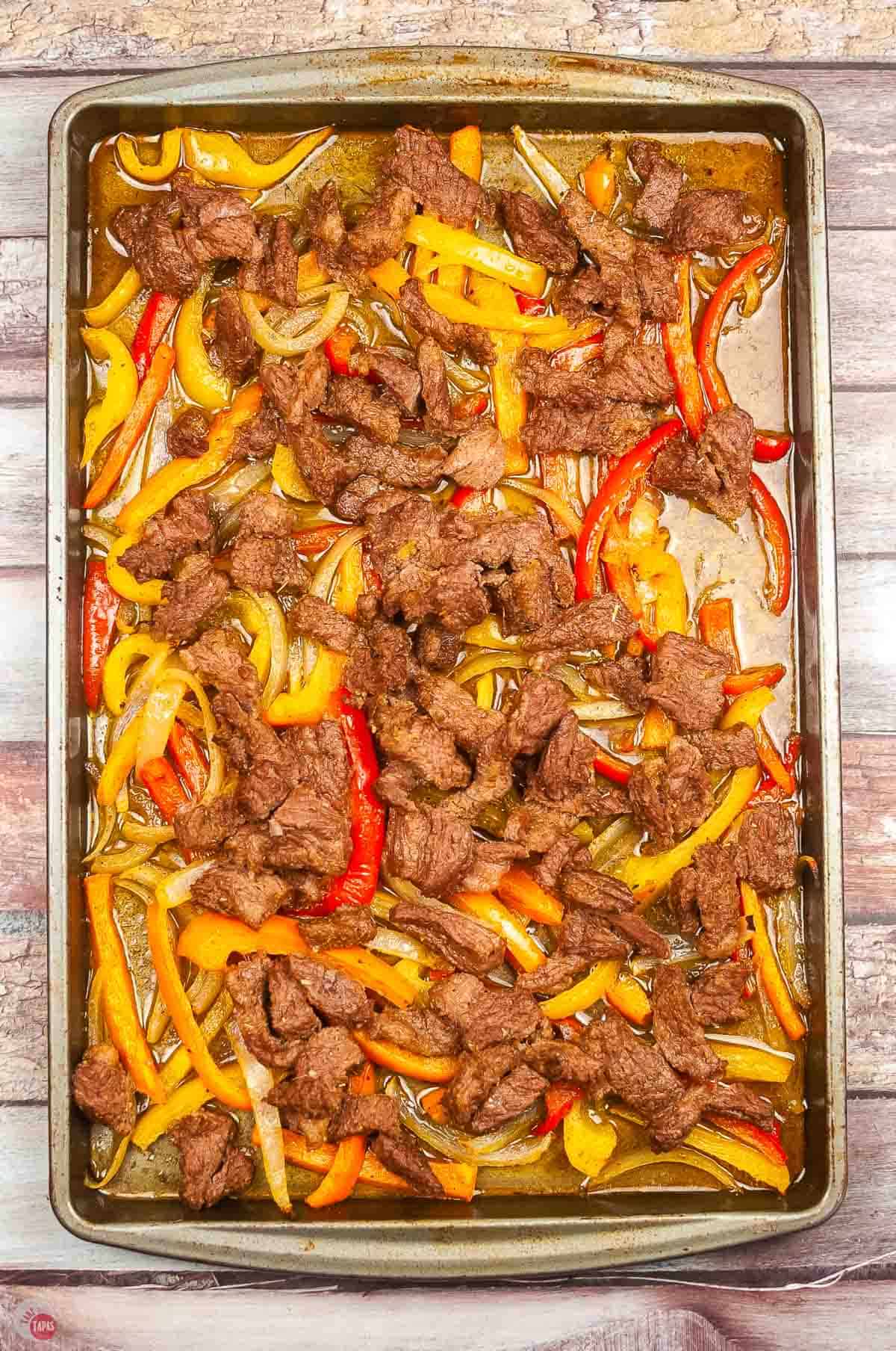 baking sheet topped with cooked steak and bell peppers and onions