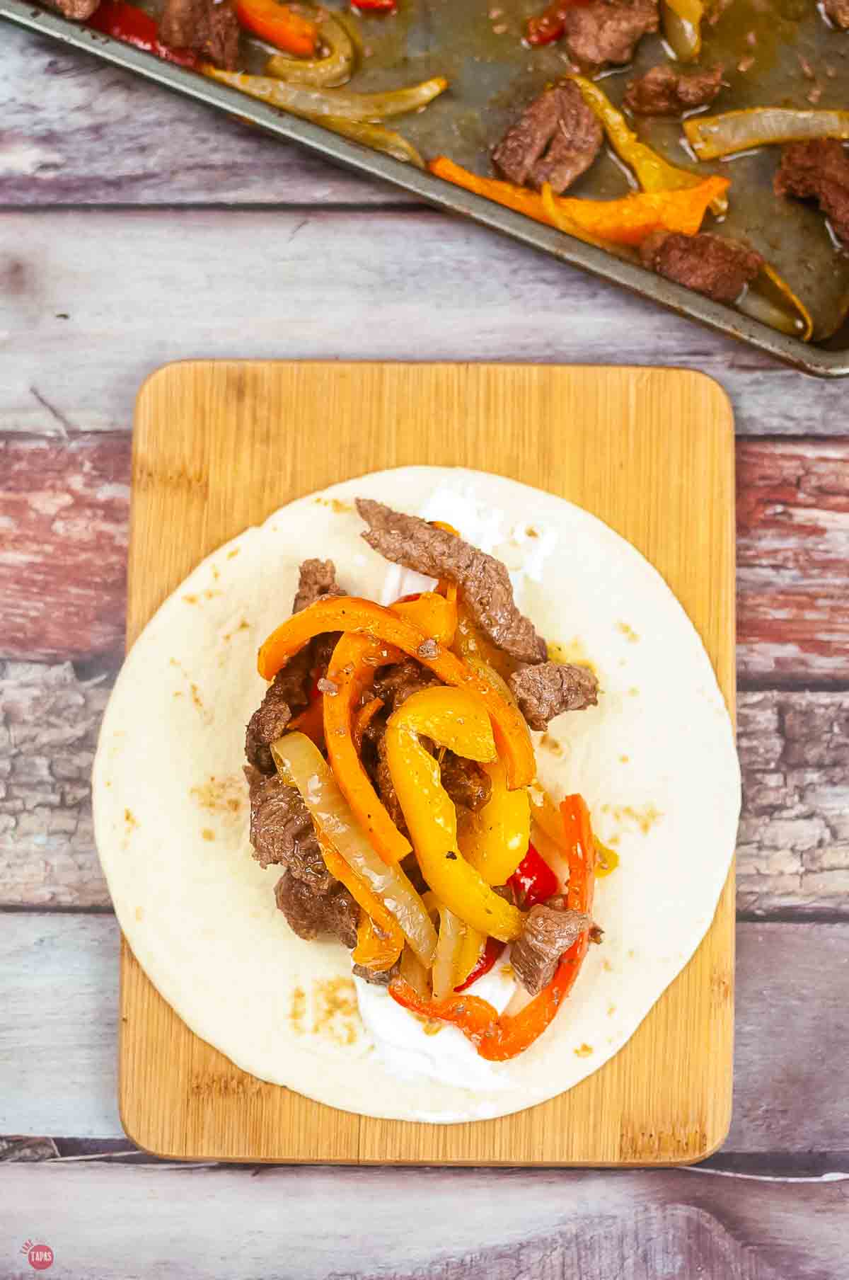 wood board topped with a tortilla filled with fajita meat and veggies