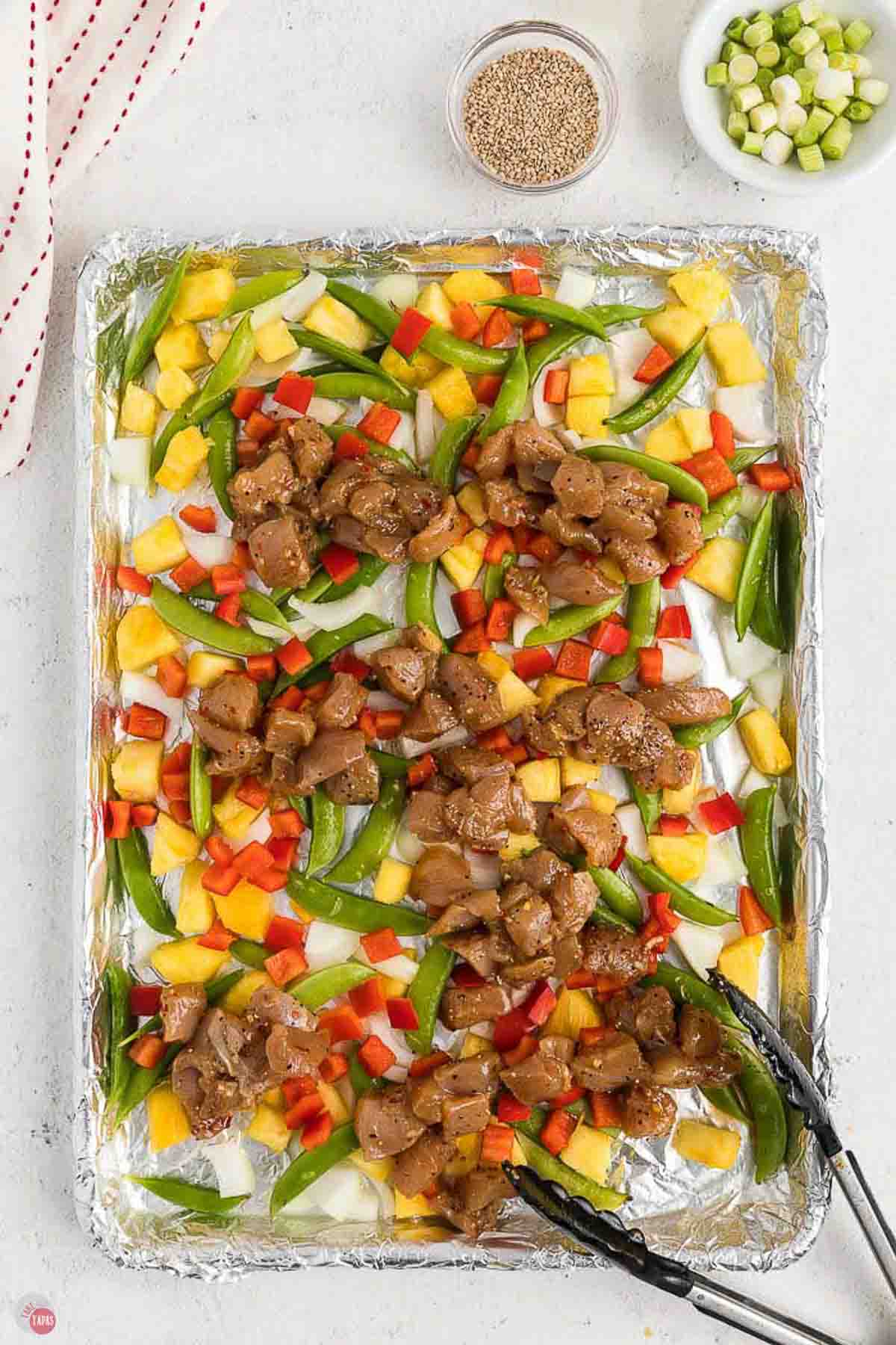 marinated chicken pieces and small pieces of vegetables on a baking sheet