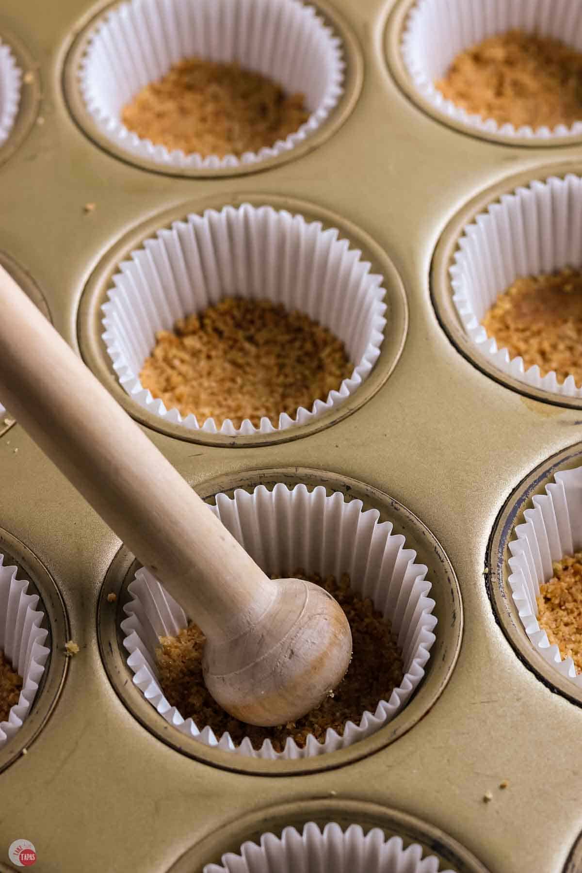 graham cracker crumbs being pressed into a cupcake liner