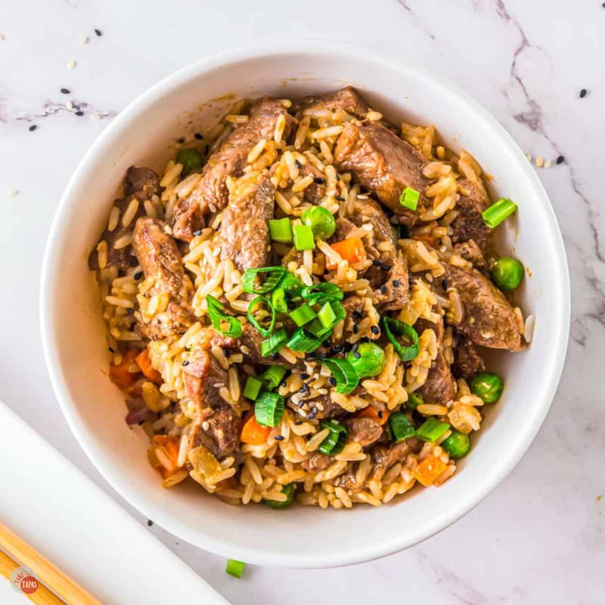 white bowl of steak fried rice with two chopsticks next to it